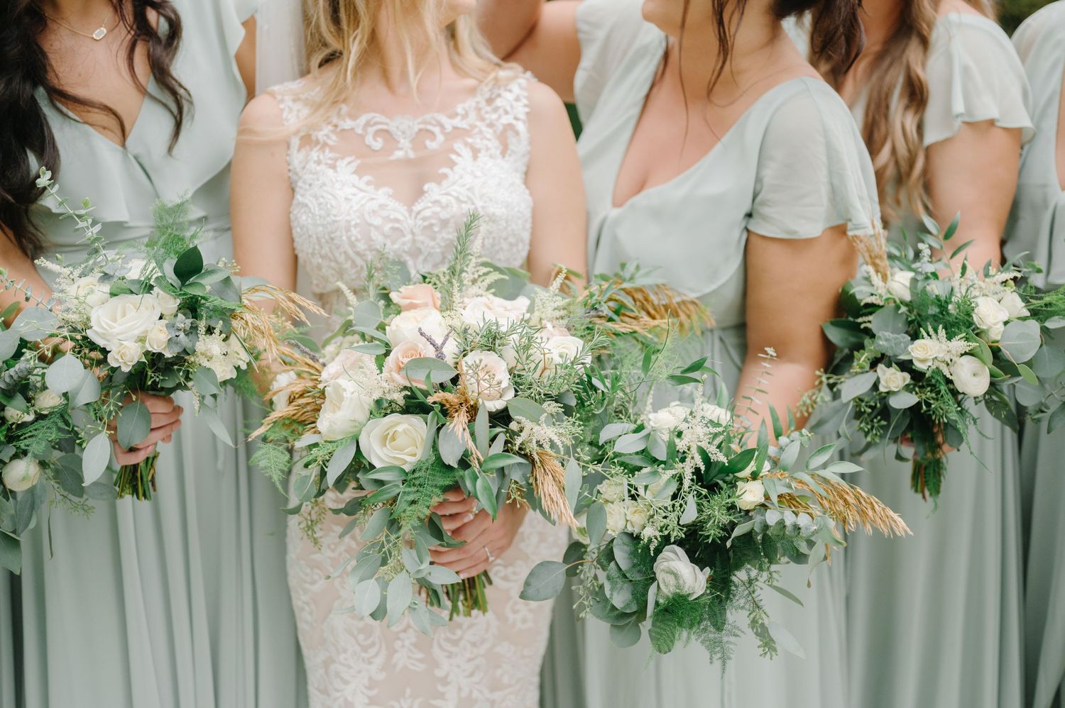 Bridesmaids in sage green dresses hold elegant bouquets of white and blush flowers with eucalyptus greenery.