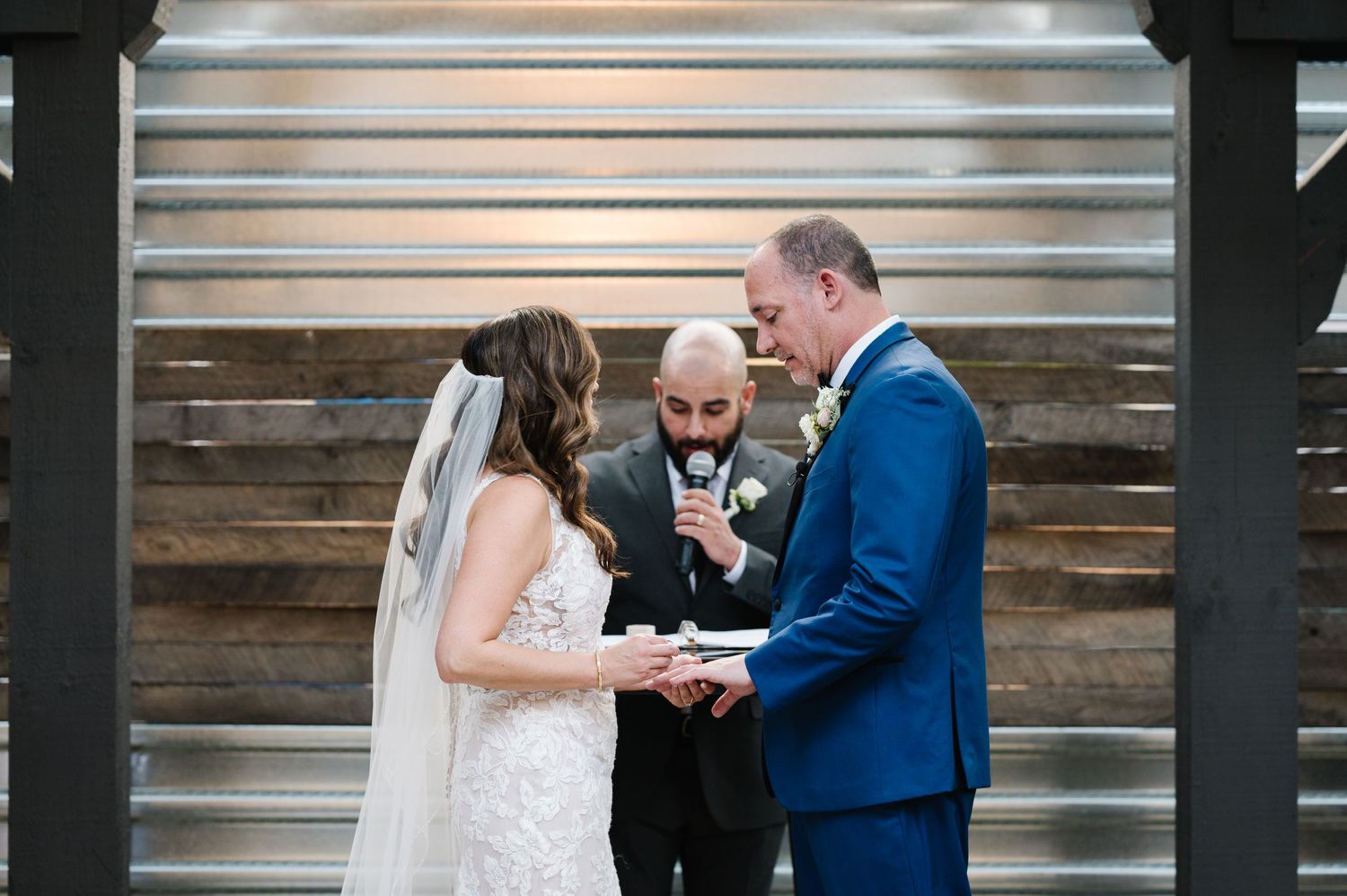 Wedding ceremony taking place in front of rustic wooden wall with silver corrugated metal panels.