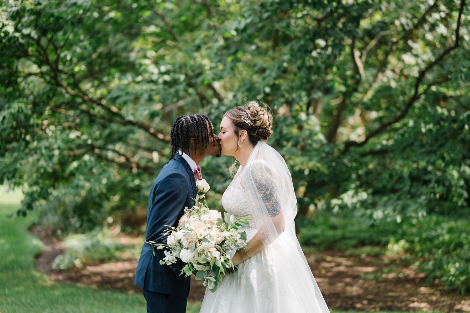 Romantic wedding couple sharing a moment in a lush garden setting with white bouquet and blue suit.