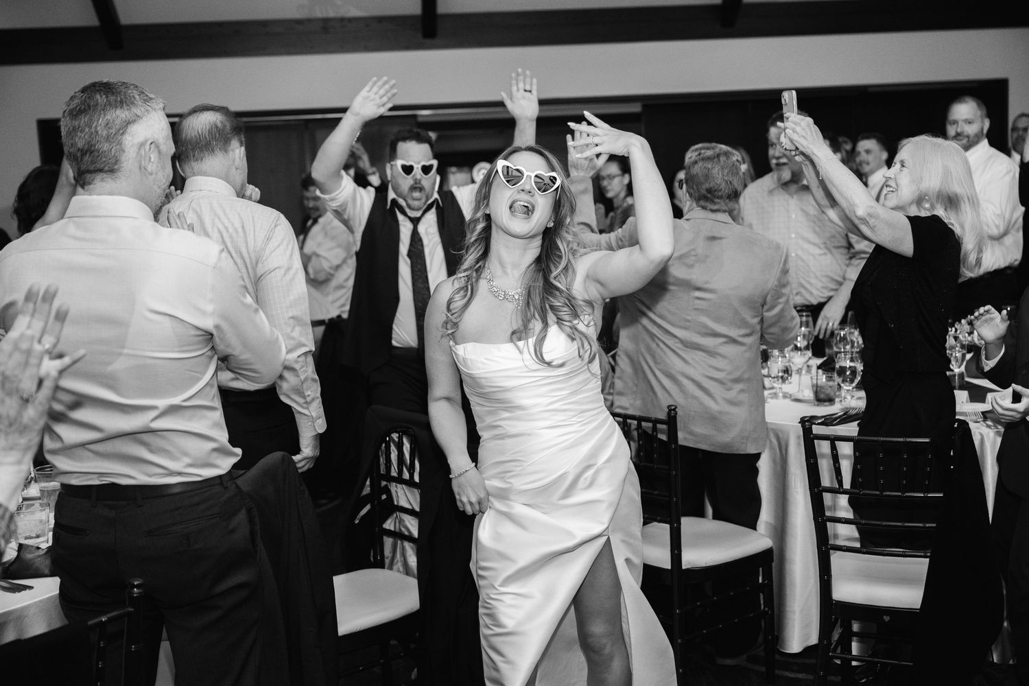 Black and white photo of energetic wedding reception dancing scene showing lively celebration on dance floor.
