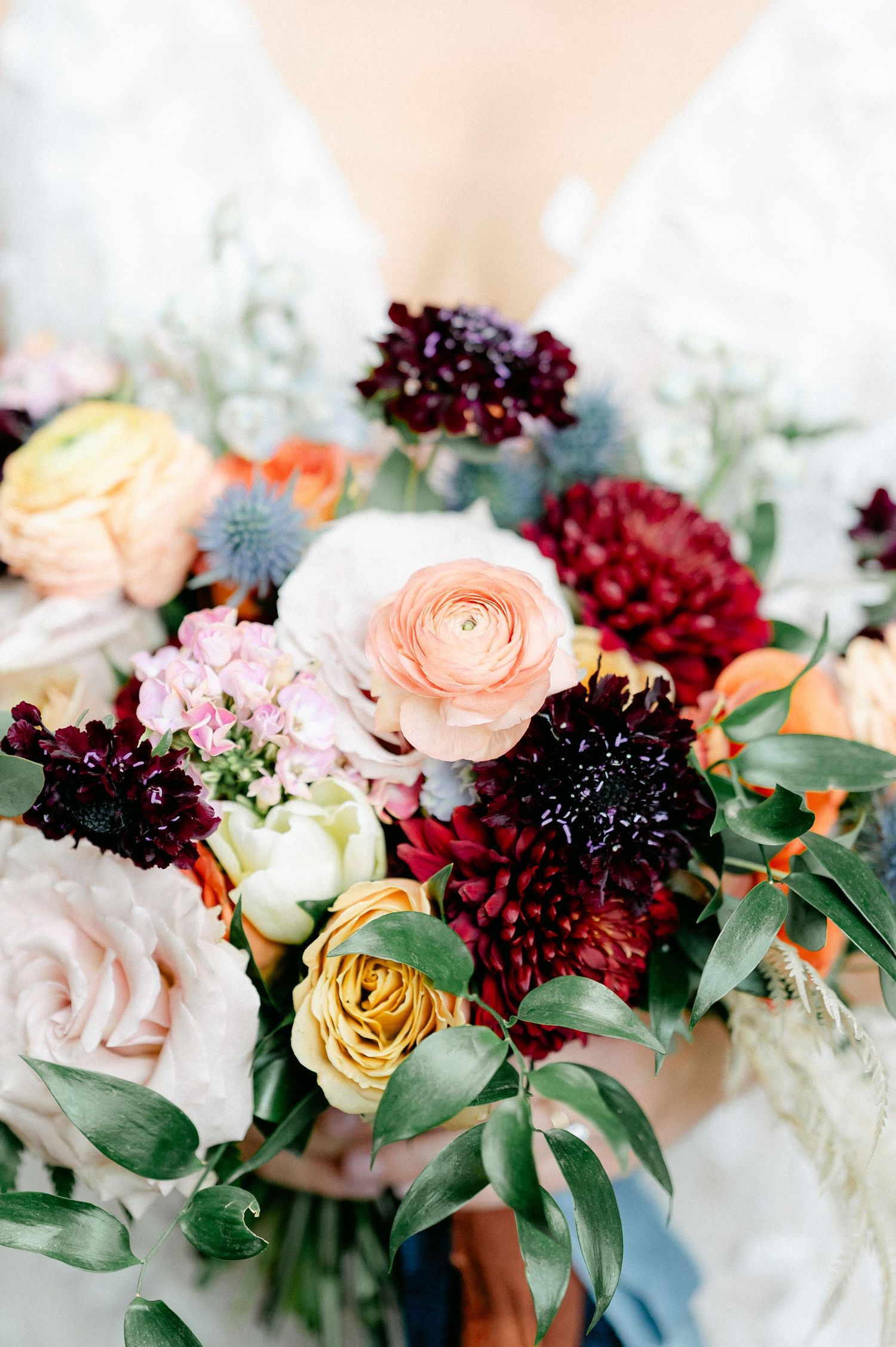 Close-up of wedding bouquet featuring peach roses, burgundy dahlias, and fresh greenery. - Hyatt Lodge Oak Brook Wedding