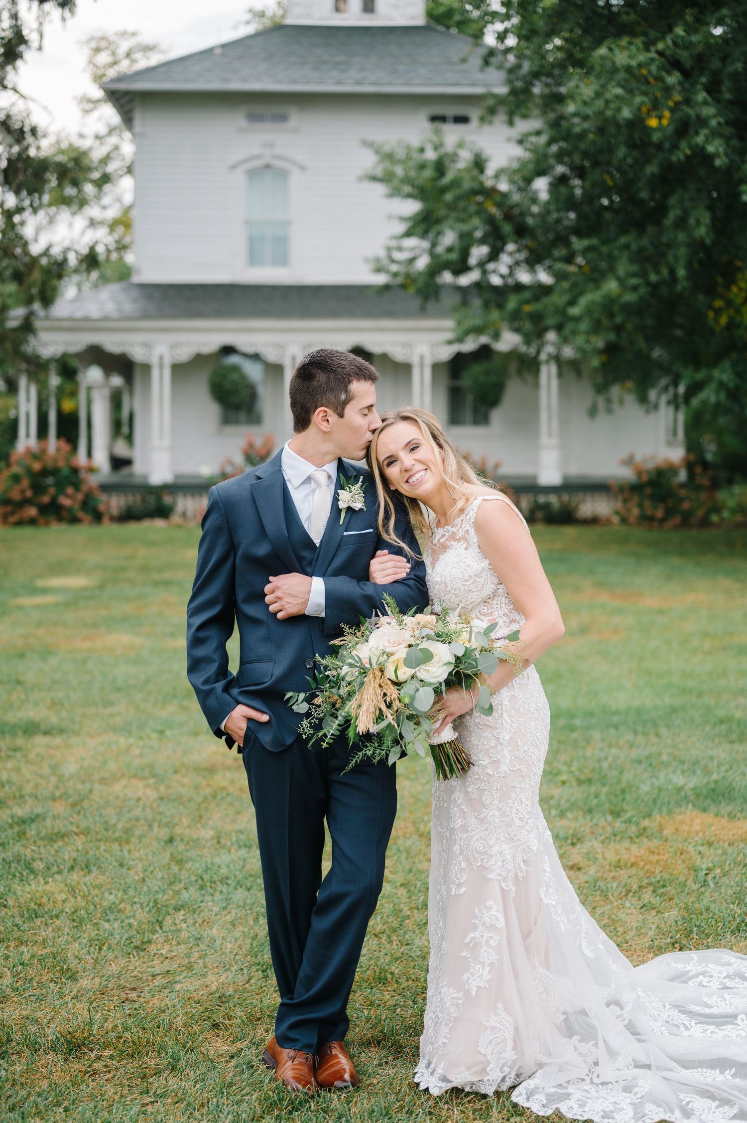 A couple shares a romantic moment in front of a white historic house. - Ashley Farm Wedding in Yorkville, IL