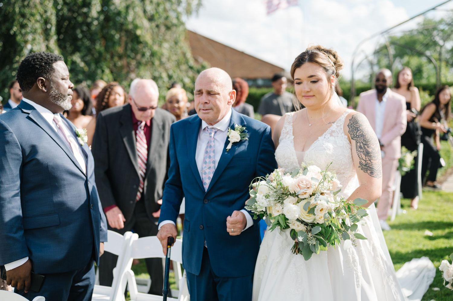 Beautiful outdoor wedding ceremony with guests in attendance as couple walks down the aisle under sunny skies.