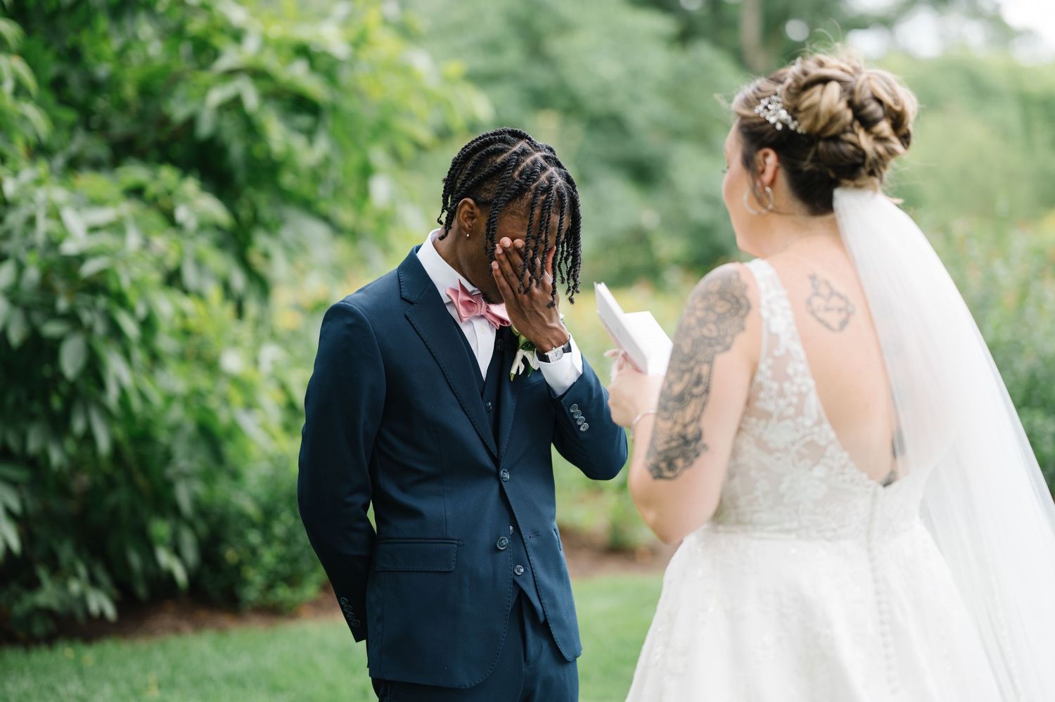 Emotional wedding photograph of a groom in navy suit and bride in lace dress sharing a candid moment outdoors.