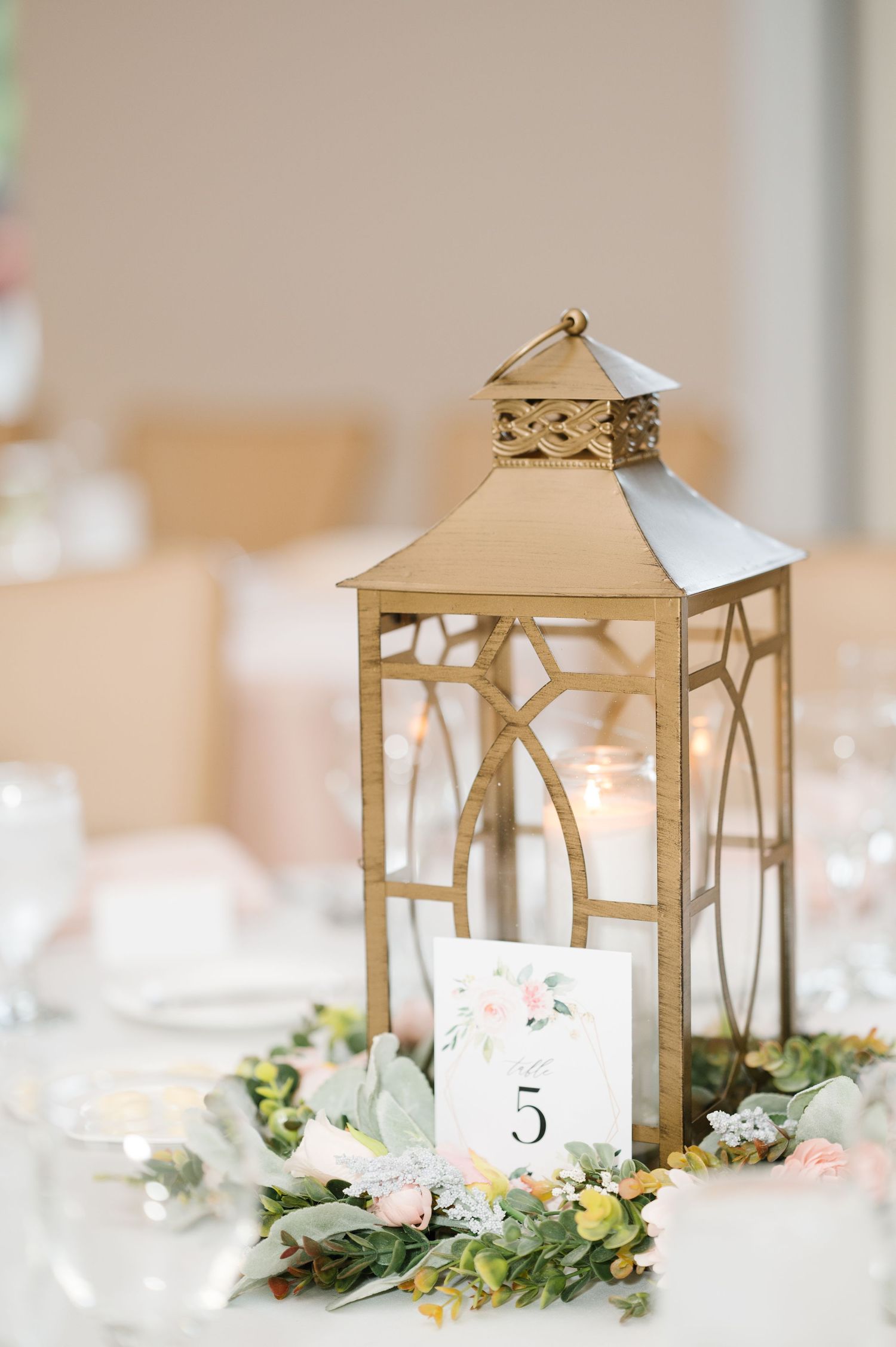 Elegant gold lantern centerpiece with table number 5 surrounded by delicate white and blush floral arrangements.