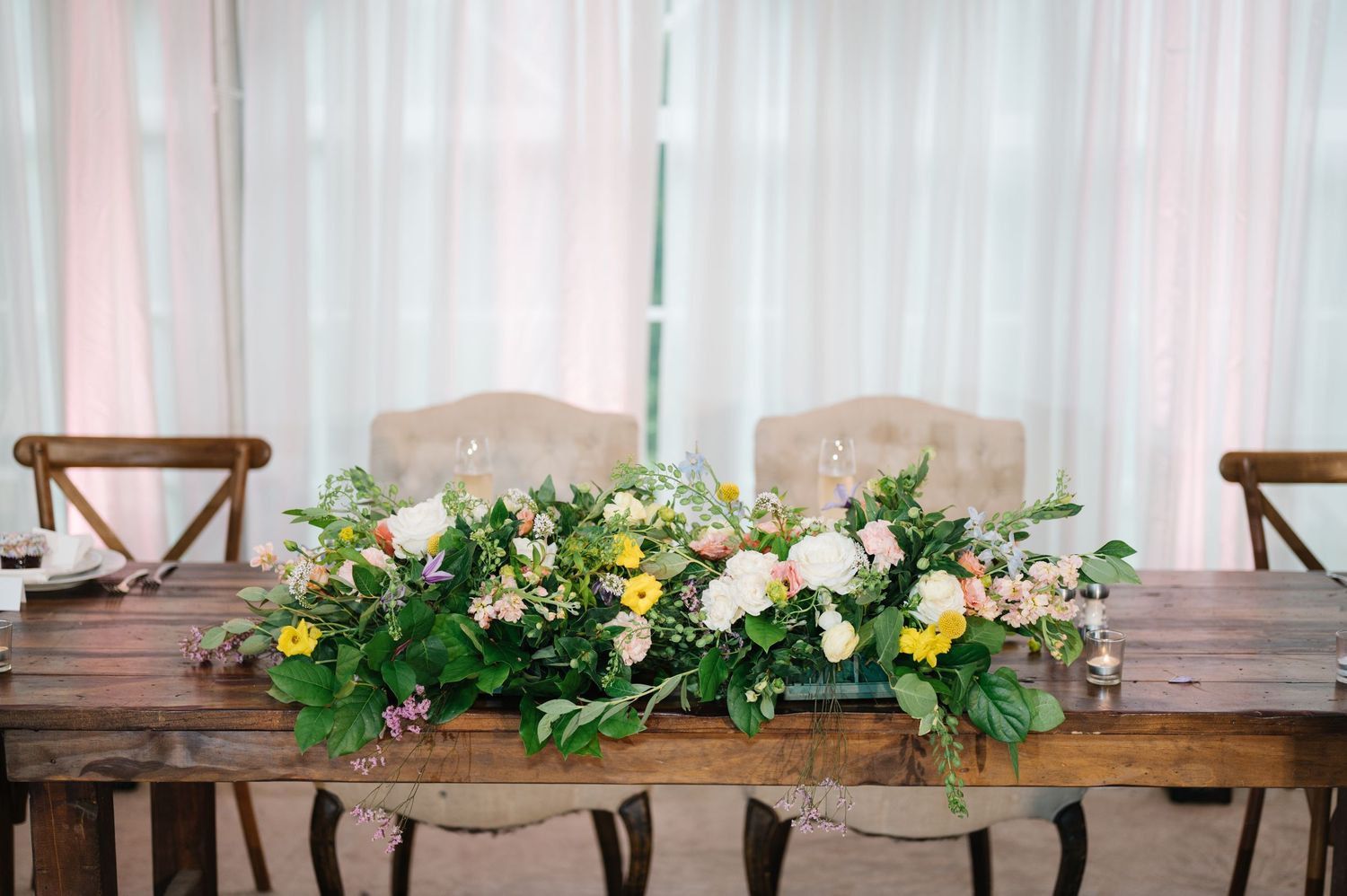 Rustic wooden farmhouse table decorated with elegant yellow and white floral centerpiece arrangement.