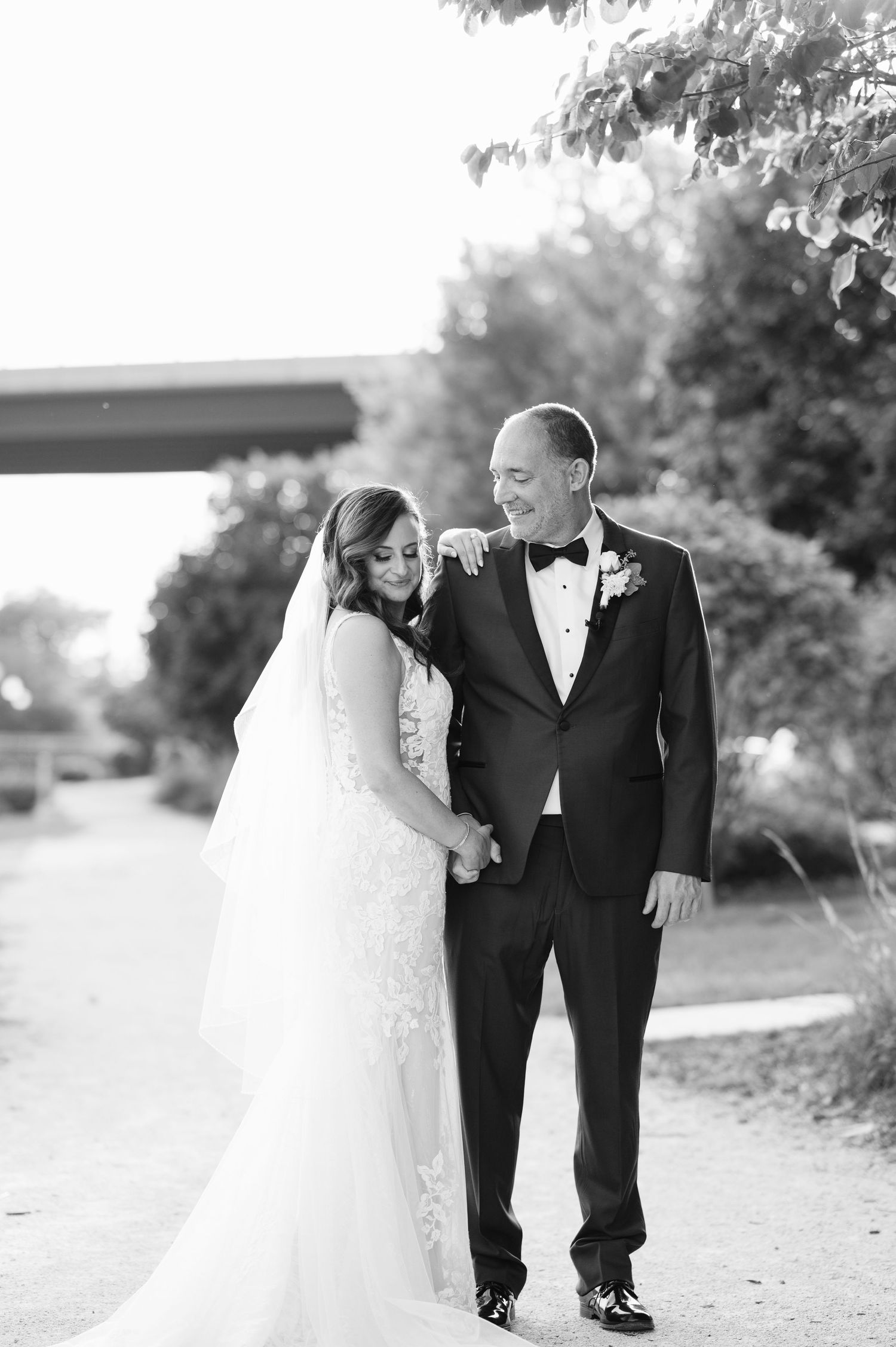 A black and white wedding photo of a couple in formal attire standing together on a path outdoors.