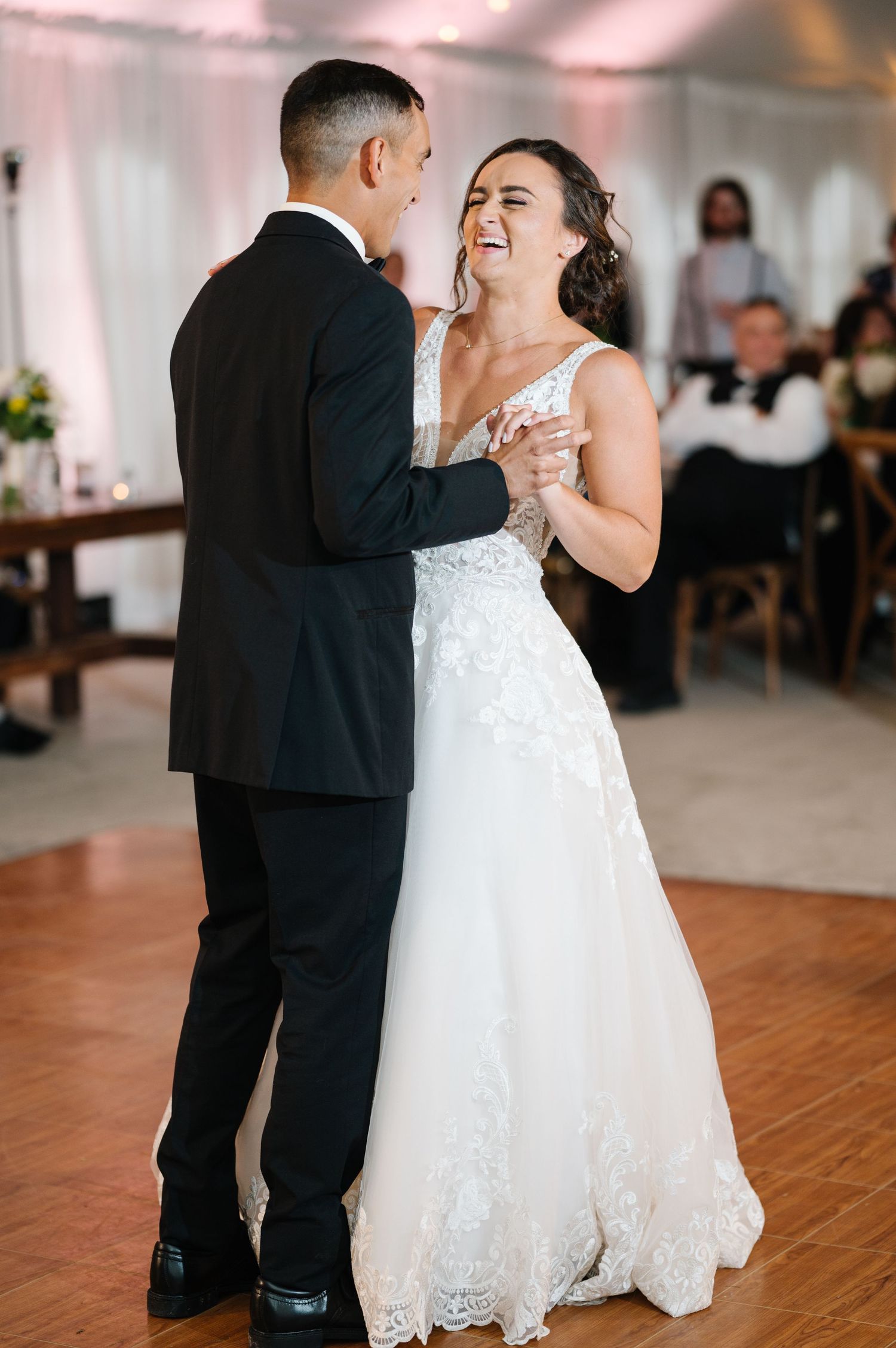 A couple shares their first dance at their wedding reception as they laugh joyfully together on the dance floor.