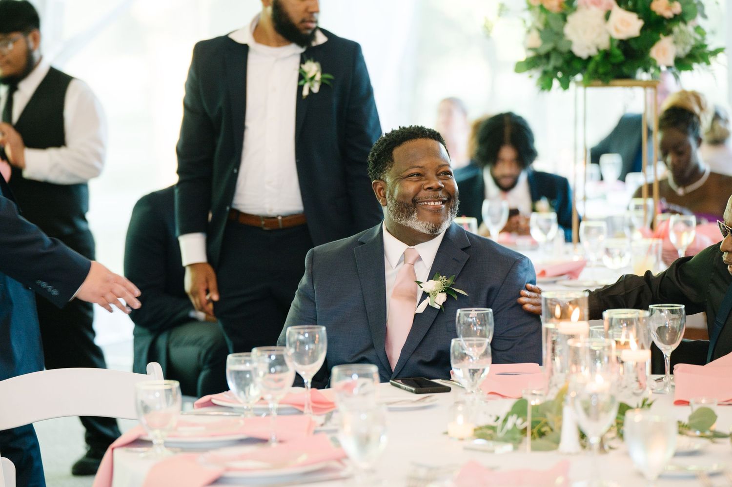 Wedding guest enjoying conversation at an elegant reception with white tablecloths and floral centerpieces.