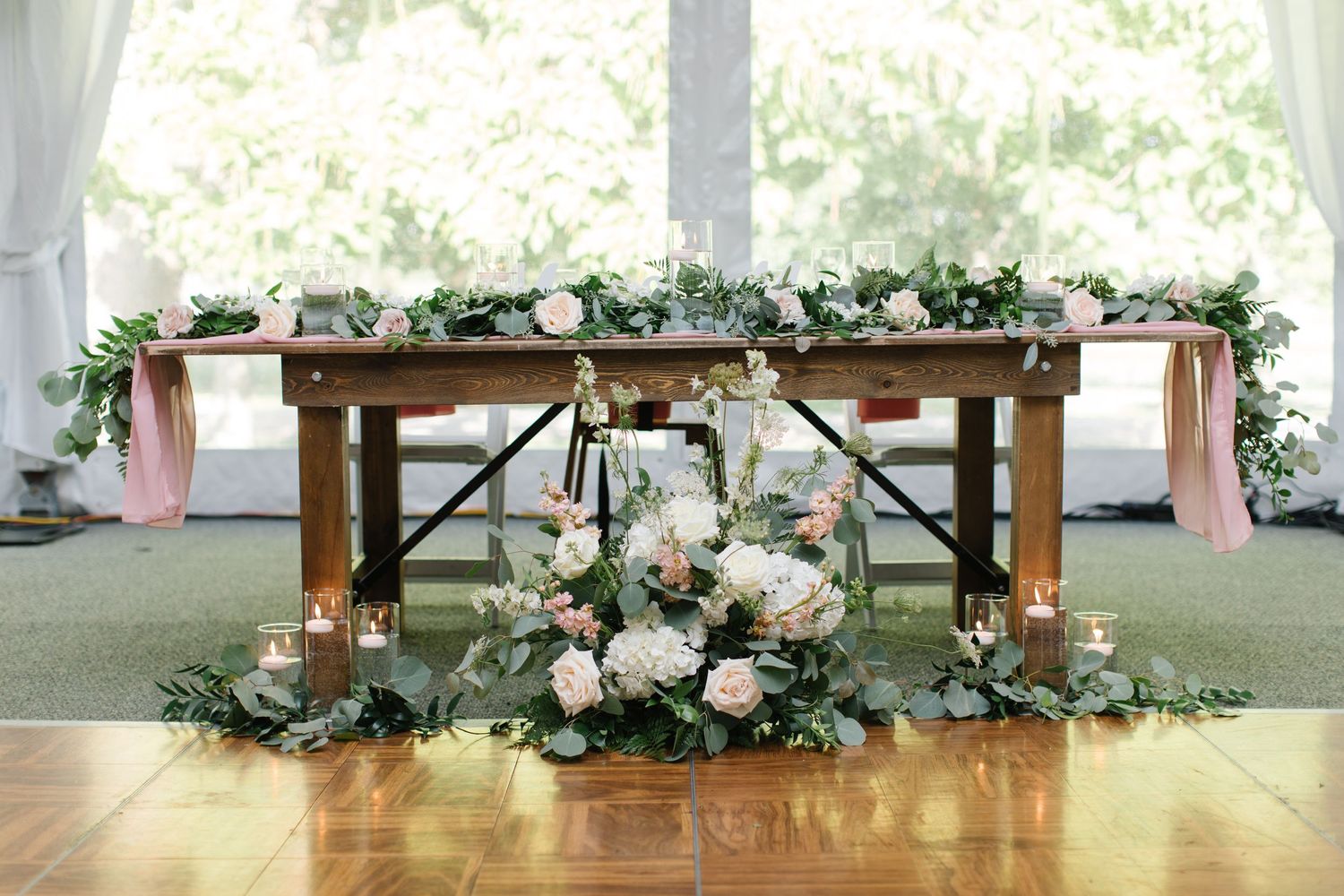Elegant rustic wedding sweetheart table decorated with pink and white floral arrangements and draped greenery garlands.