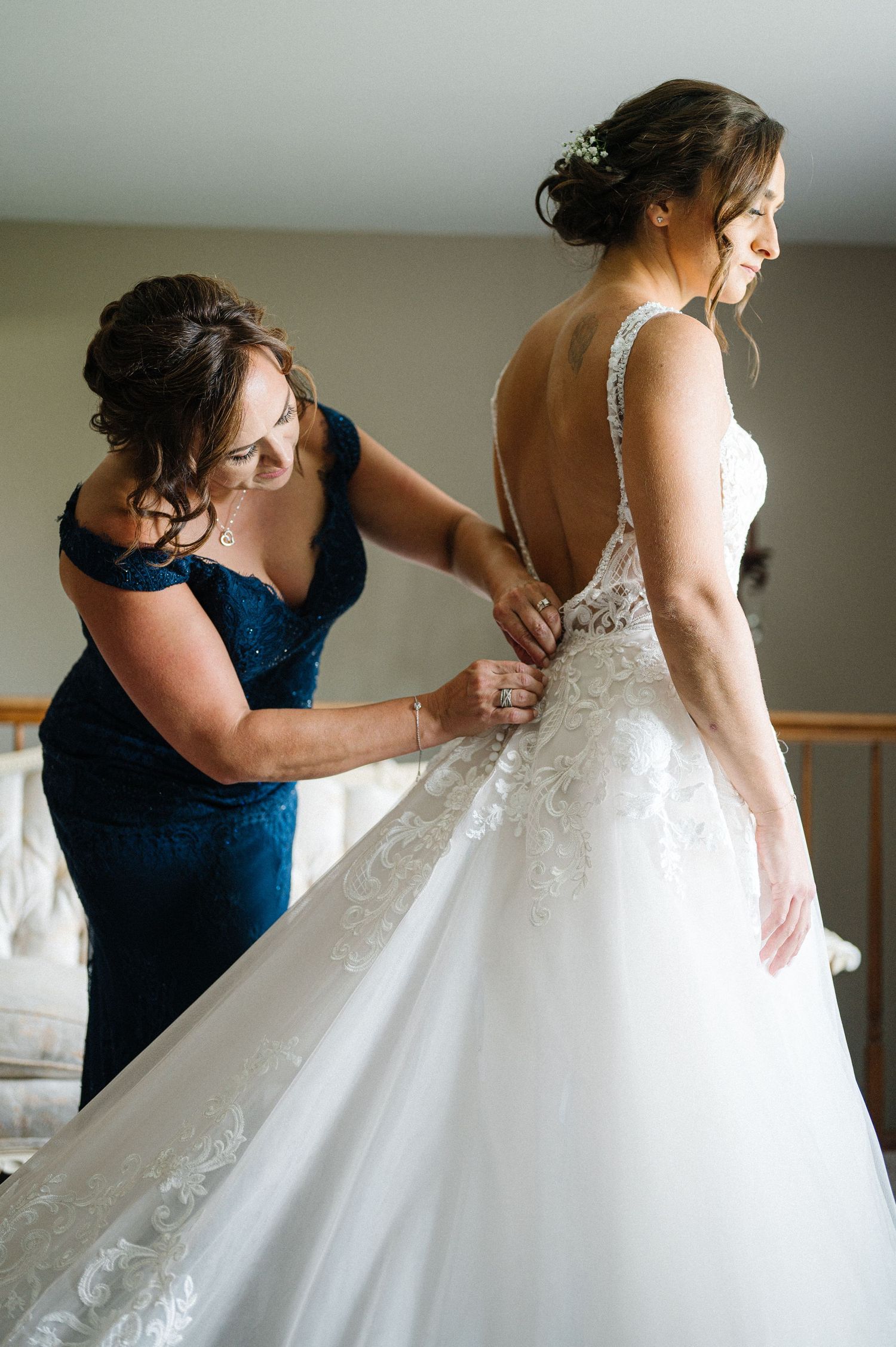 A bridesmaid in navy blue helps adjust a beautiful white lace wedding dress during pre-ceremony preparations.