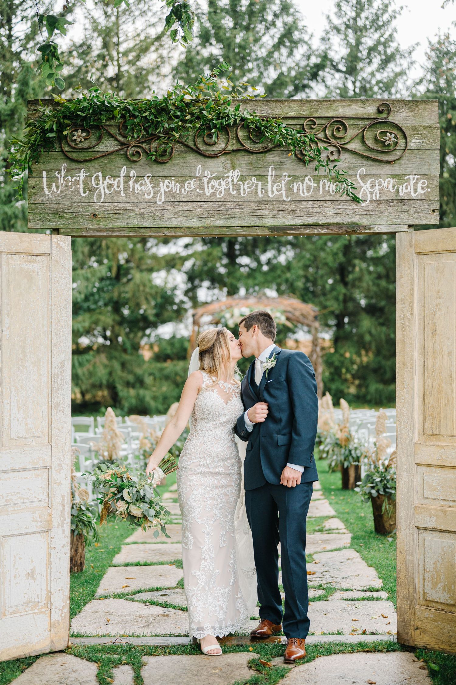 A romantic garden wedding ceremony entrance with vintage doors, stone path, and decorative greenery arch.