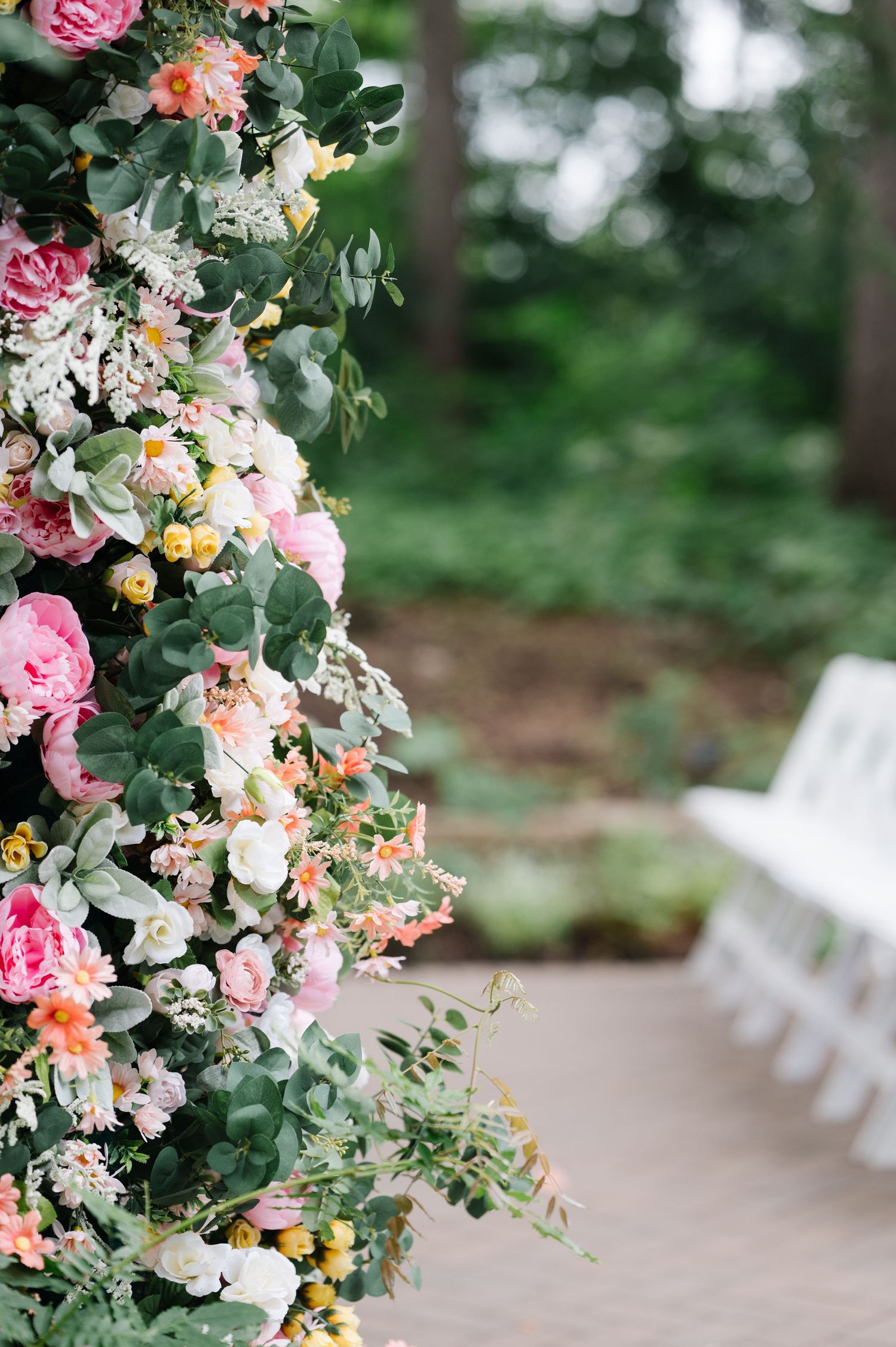 Elegant floral arch with pink roses, eucalyptus, and mixed blooms stands before white ceremony chairs in an outdoor garden setting.