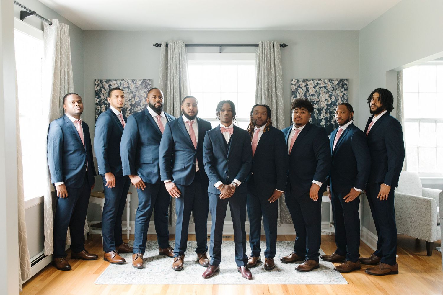 A group in coordinated navy blue suits and formal attire poses together in a bright room with white walls.