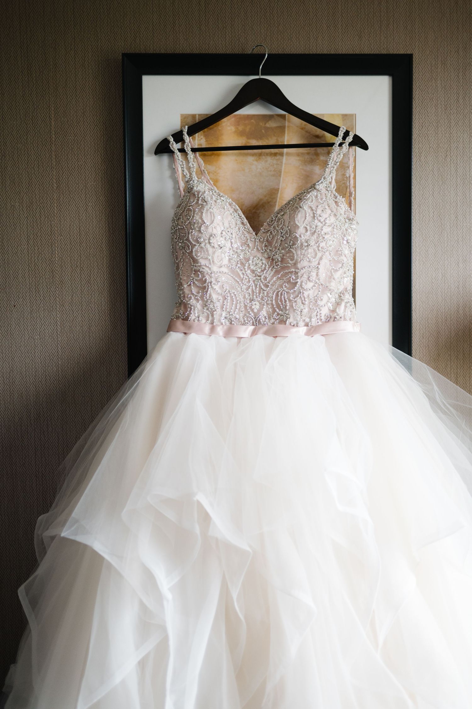 Elegant white wedding dress with lace bodice and tulle skirt hanging on black hanger against grey wall.
