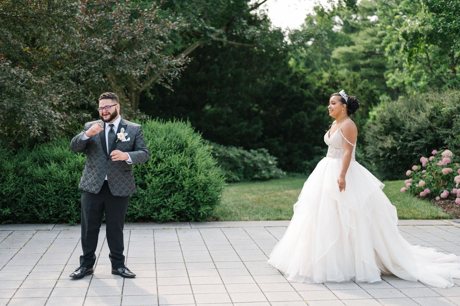 Emotional first look between newlyweds at outdoor garden wedding with lush greenery and stone patio.