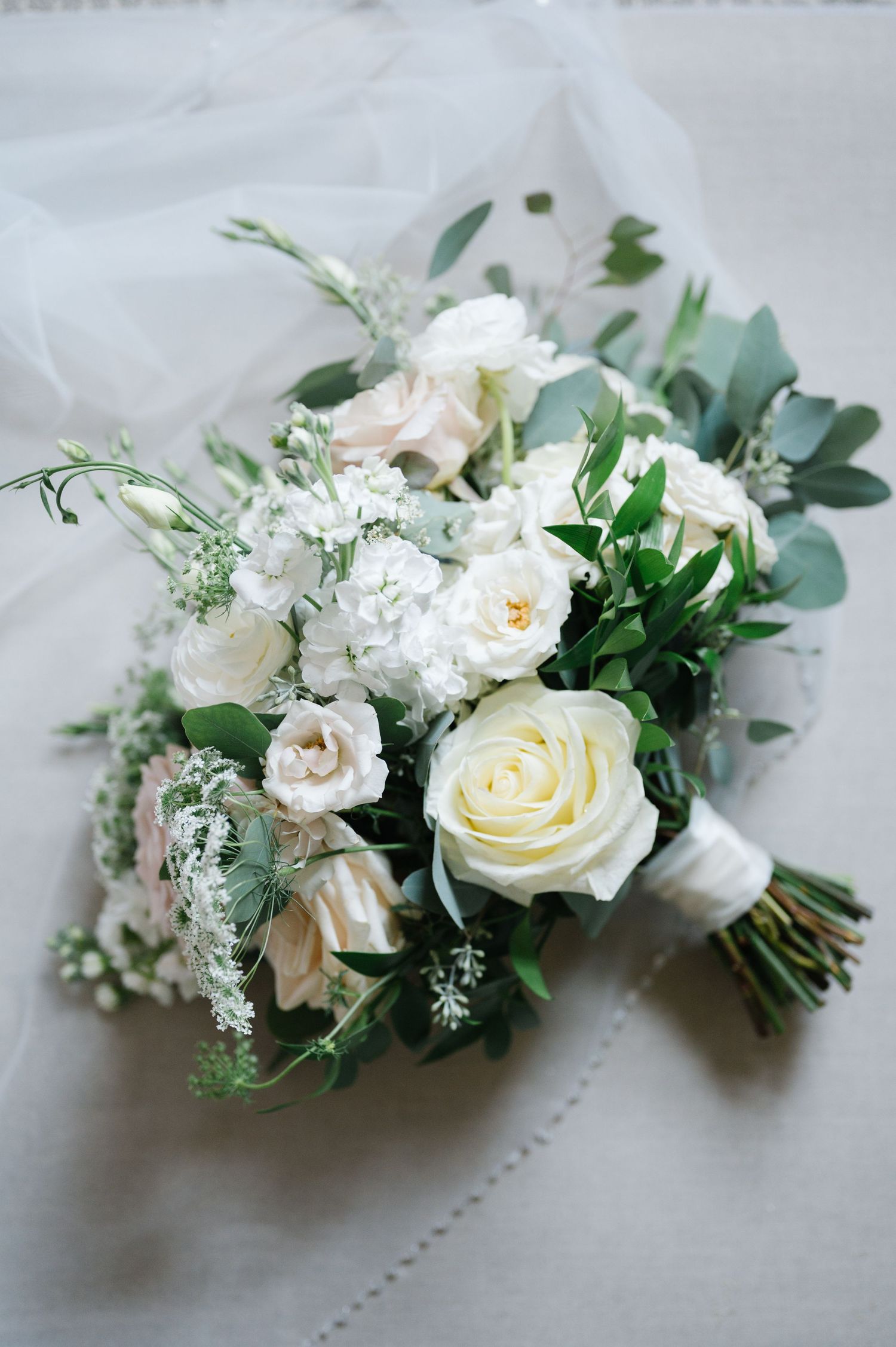 A delicate bridal bouquet featuring white roses, eucalyptus leaves, and baby's breath arranged on light fabric.