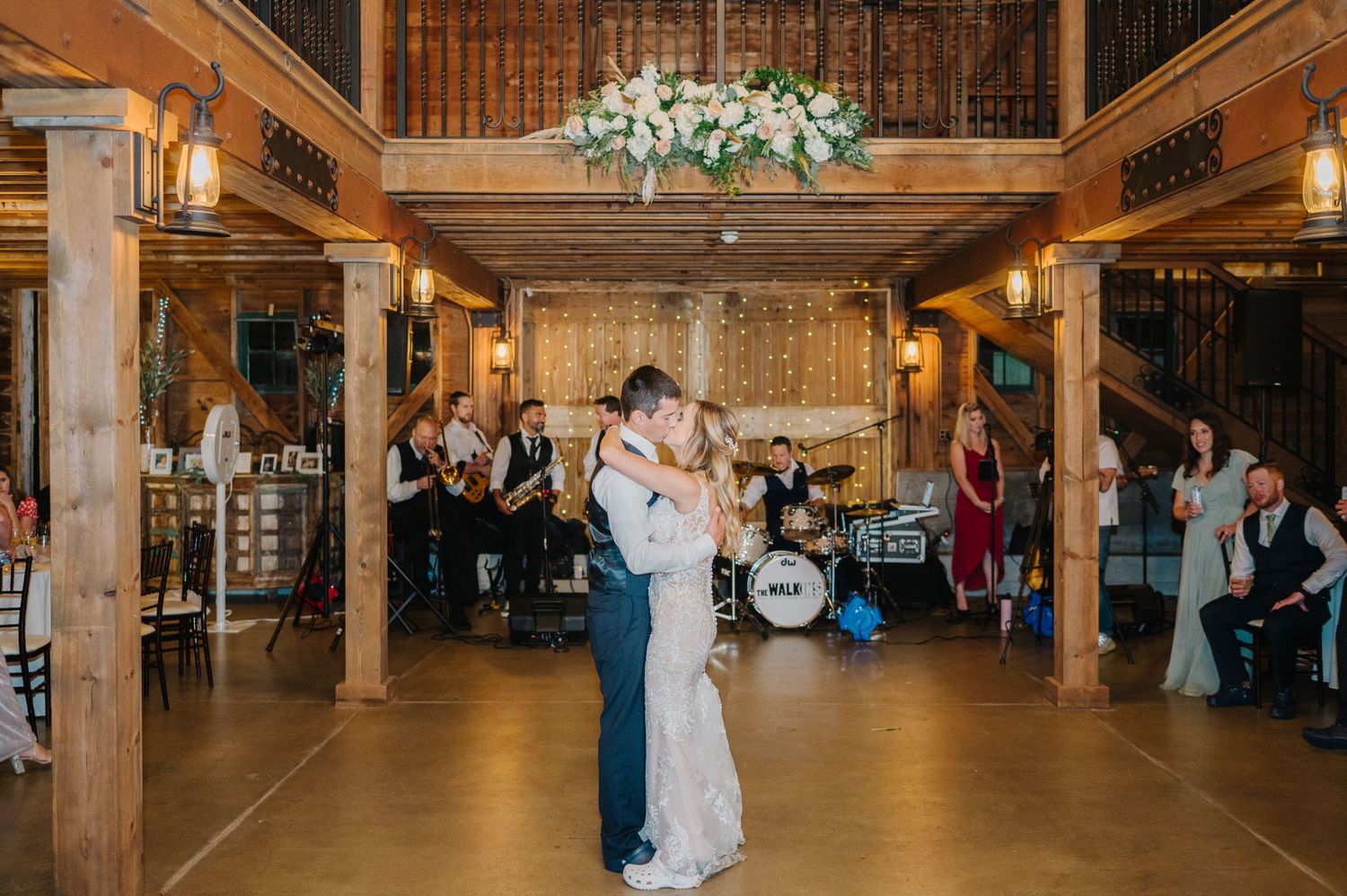 A couple shares their first dance at a rustic barn reception venue with wooden pillars and romantic lighting.