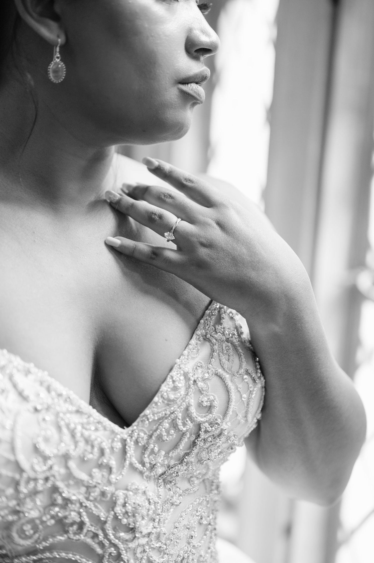 Elegant black and white photo showing delicate lace wedding dress detail and jewelry with soft window light.