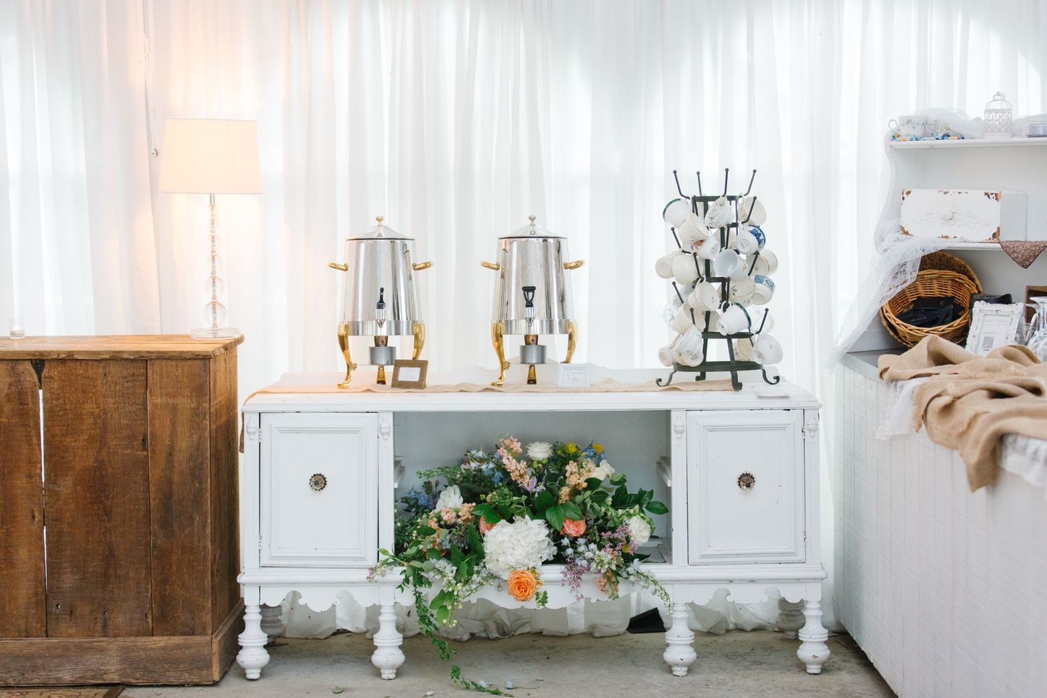 Elegant white vintage buffet cabinet decorated with crystal drink dispensers and floral arrangement in soft tones.