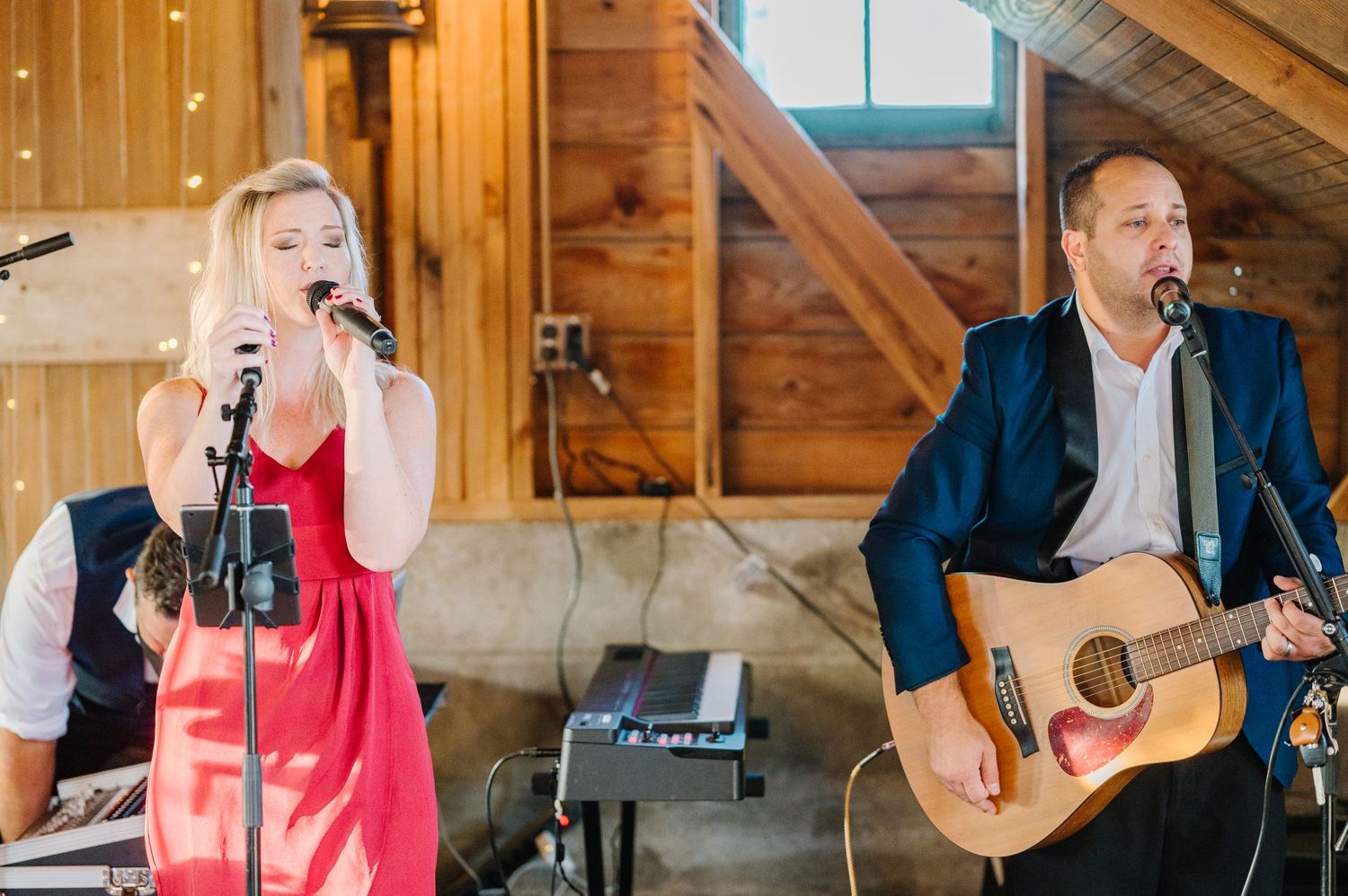 Musicians perform as a duo on stage with an acoustic guitar and microphone in a rustic wooden venue.