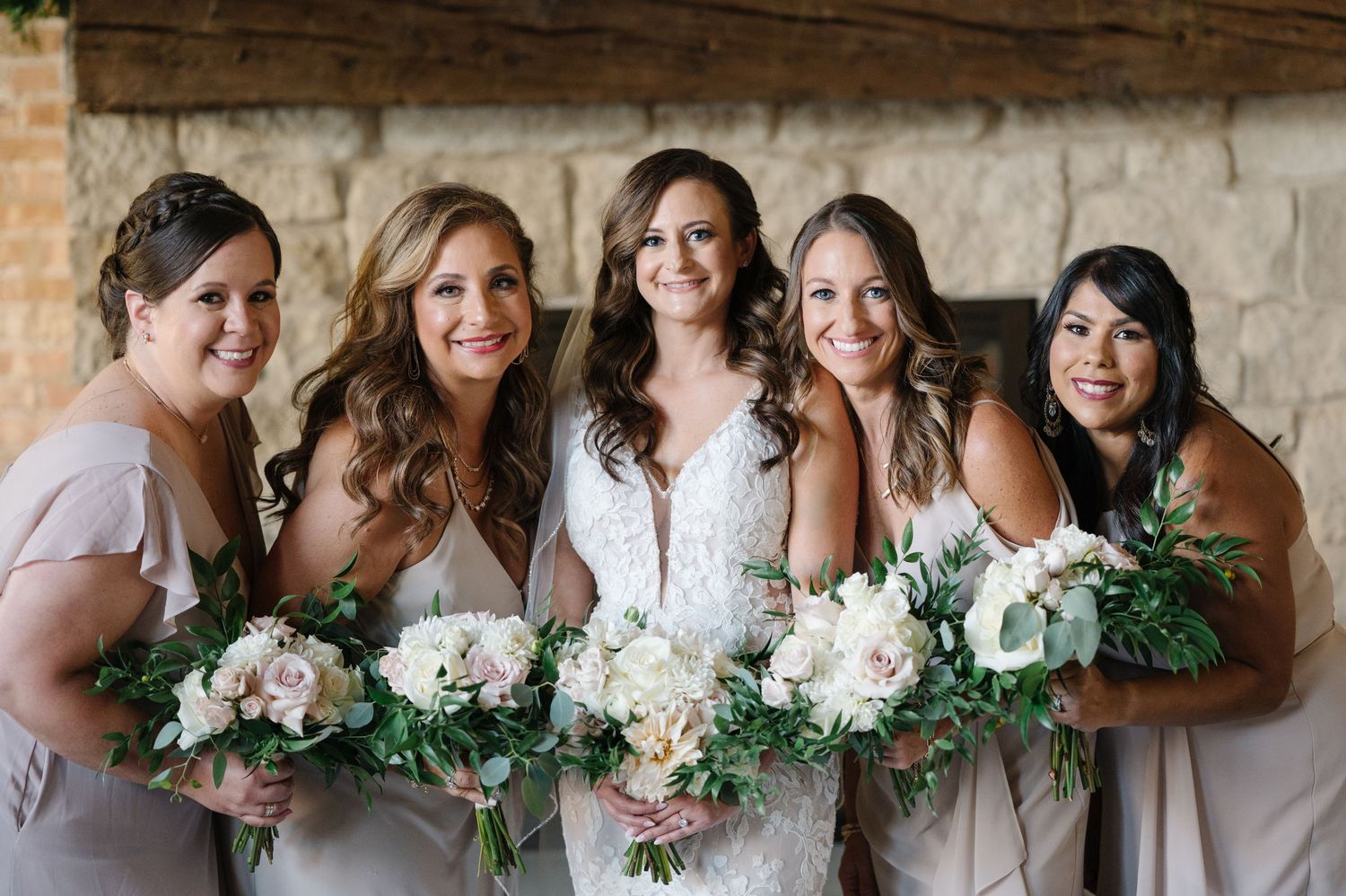 Bridesmaids in soft blush dresses holding beautiful white and pink floral bouquets at rustic stone venue.
