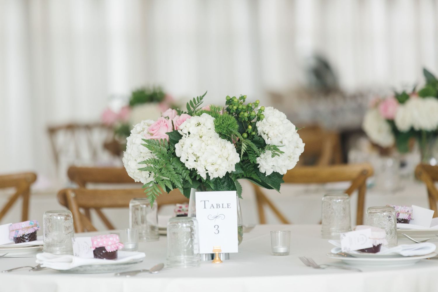 Elegant wedding reception table centerpiece with pink and white hydrangeas in a white vase alongside table settings.