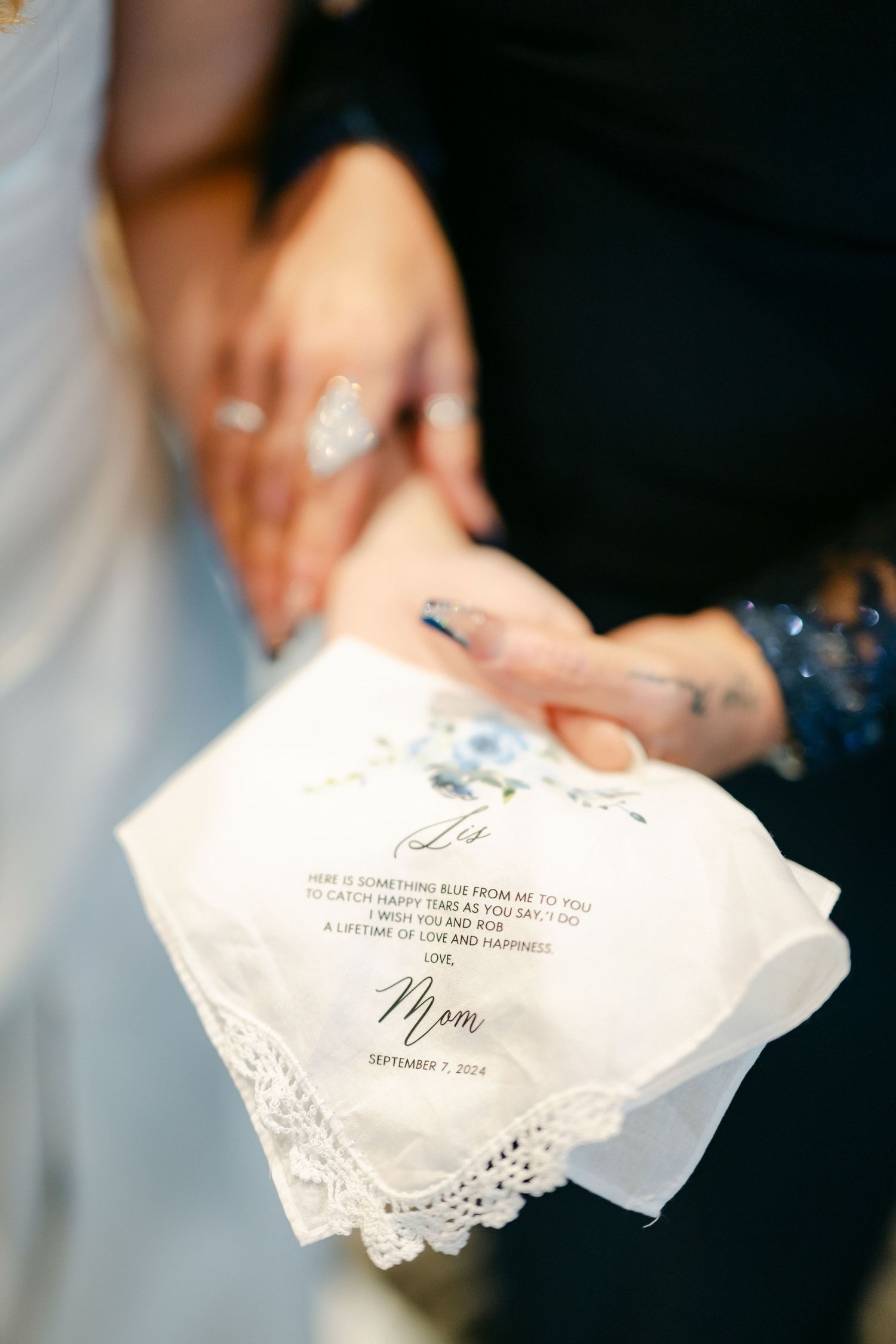 A delicate white lace-trimmed handkerchief with custom text, held in hands during a wedding ceremony.