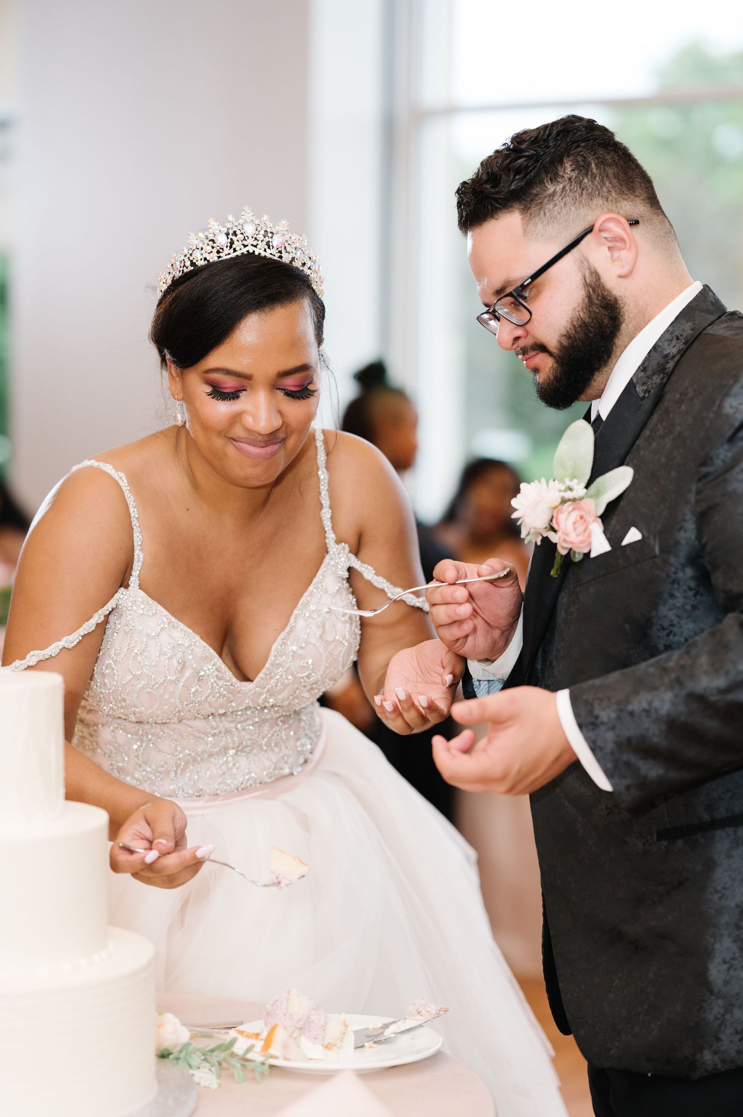 A newlywed couple shares a sweet moment while cutting into their wedding cake at an elegant indoor reception.