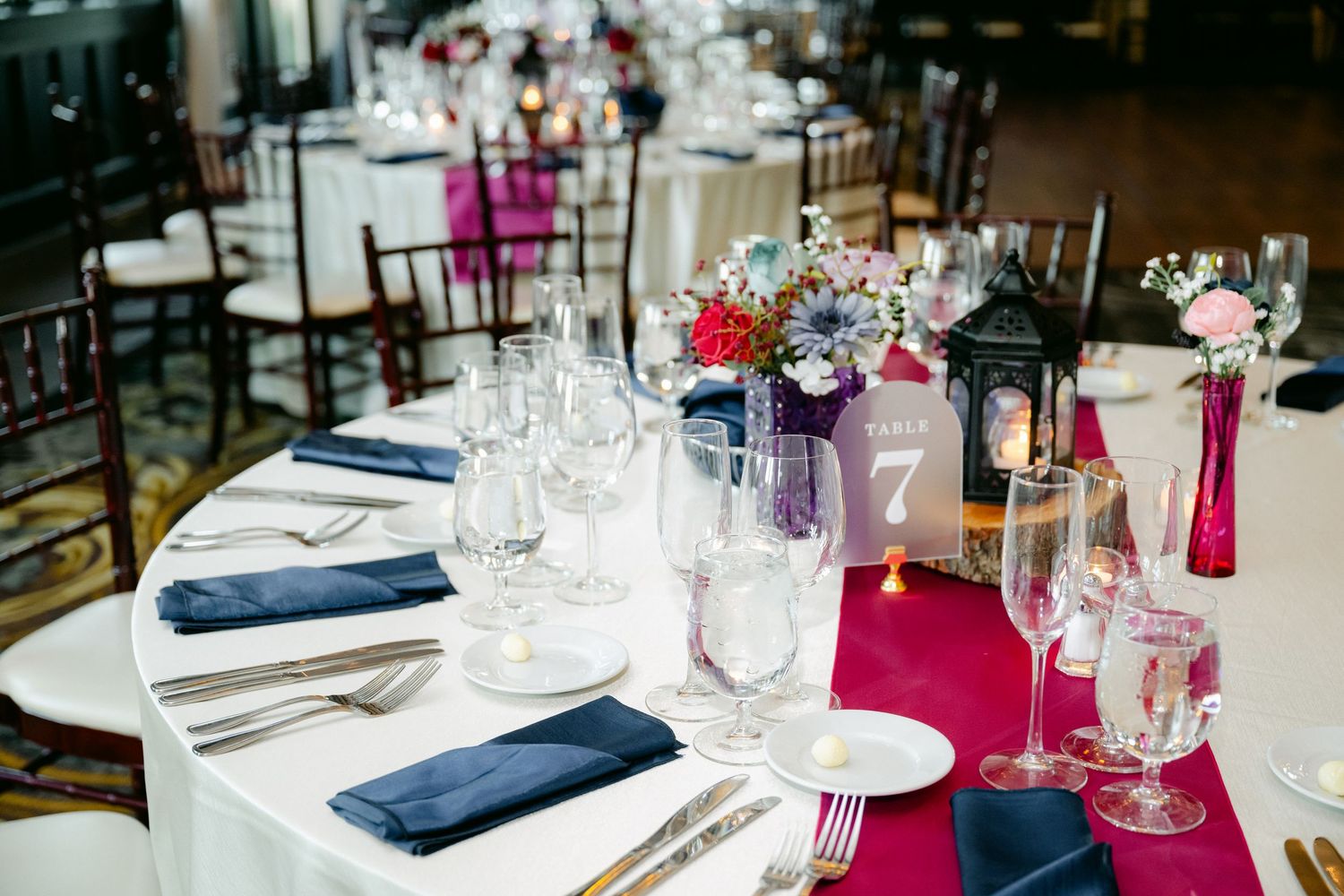 Elegant wedding reception table setting with navy blue napkins and pink accents featuring colorful floral centerpieces.