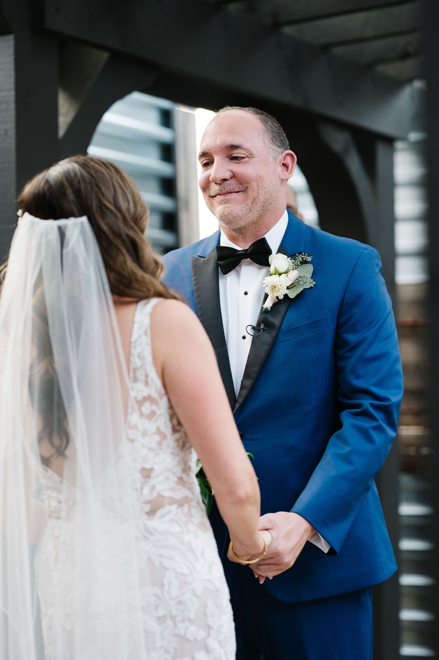A joyful moment between newlyweds as they gaze at each other, with the groom wearing a bright blue suit and bowtie.