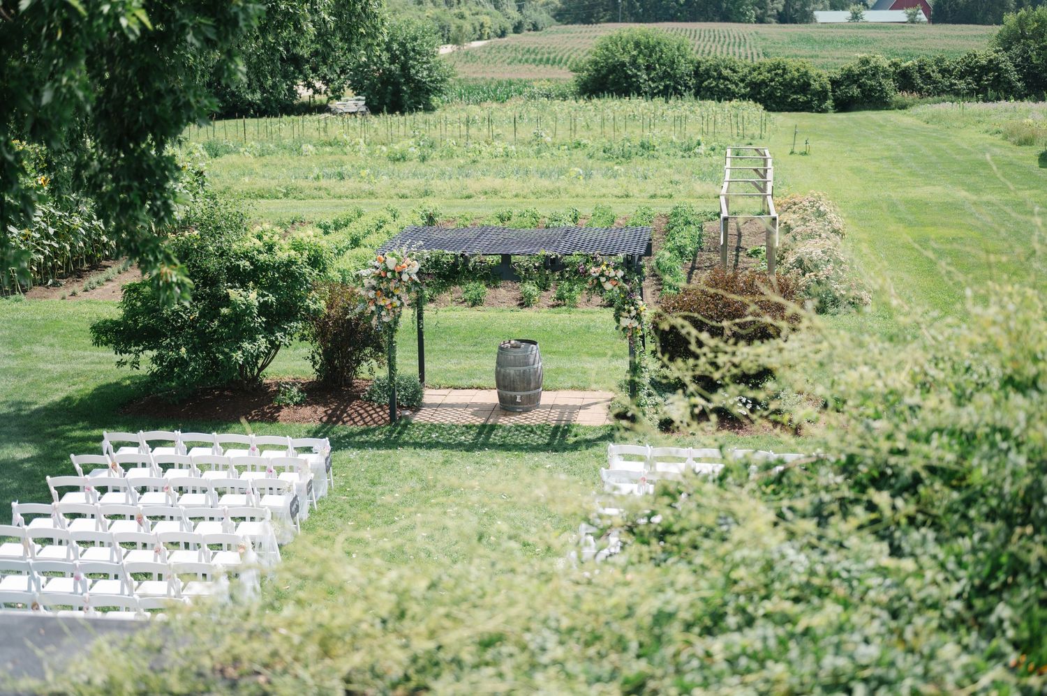 White folding chairs arranged on a grassy lawn for an outdoor wedding ceremony with rustic wooden arch.