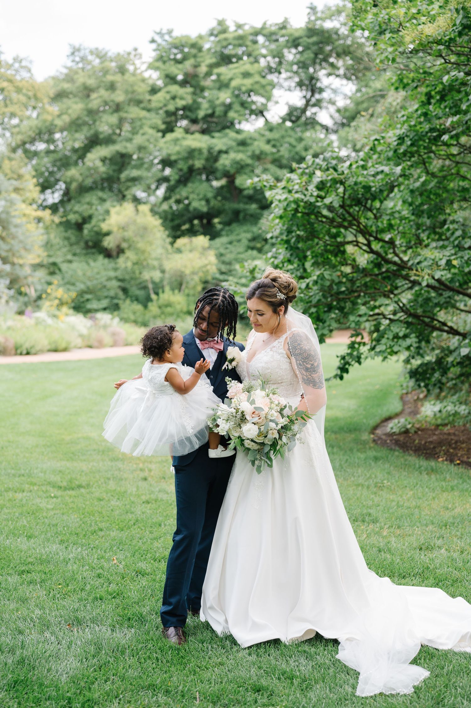 A wedding celebration outdoors on a lush green lawn surrounded by leafy trees during a summer day.