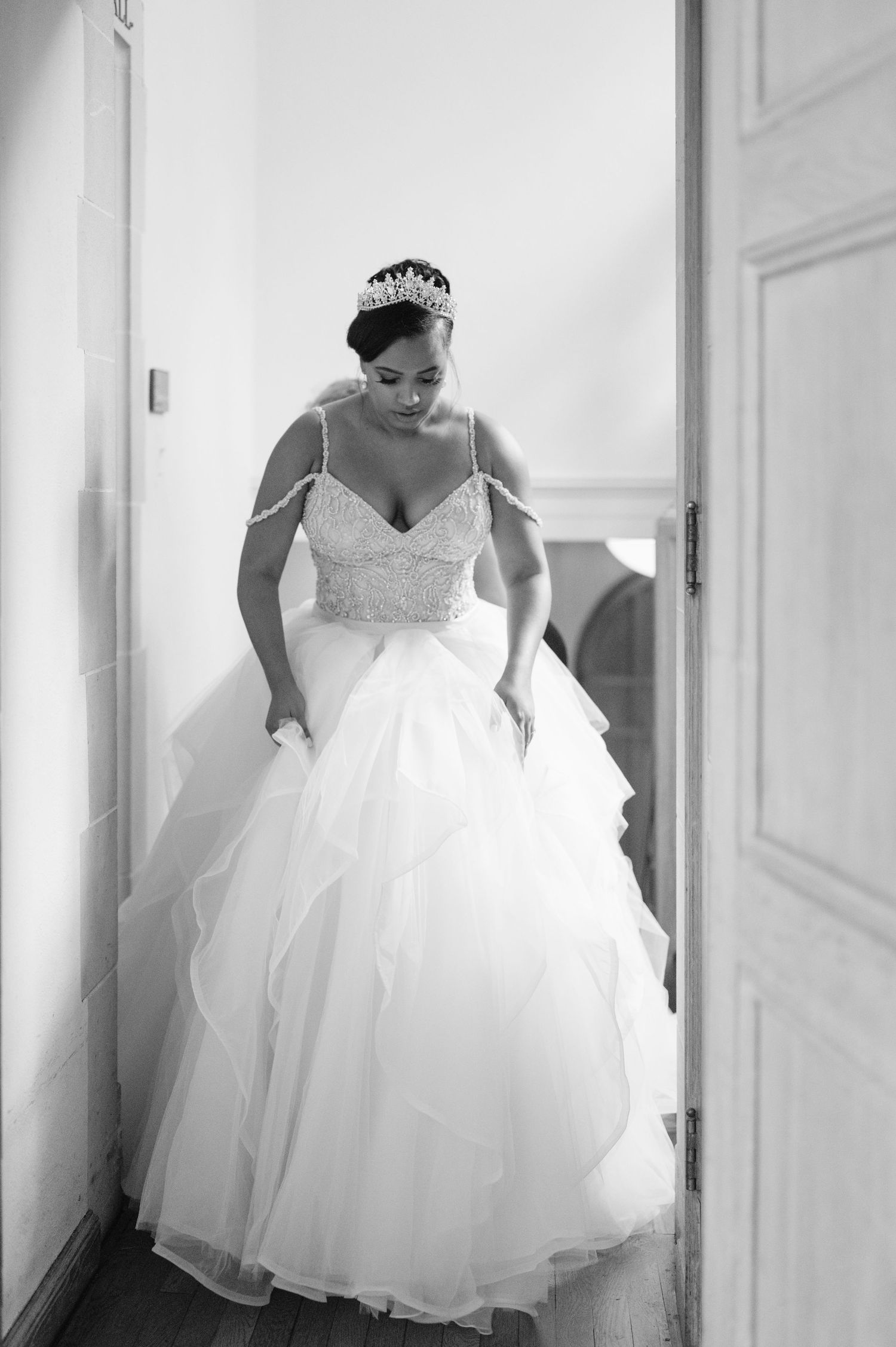 A stunning black and white photograph of a bride in a full tulle ball gown and tiara standing in a doorway.