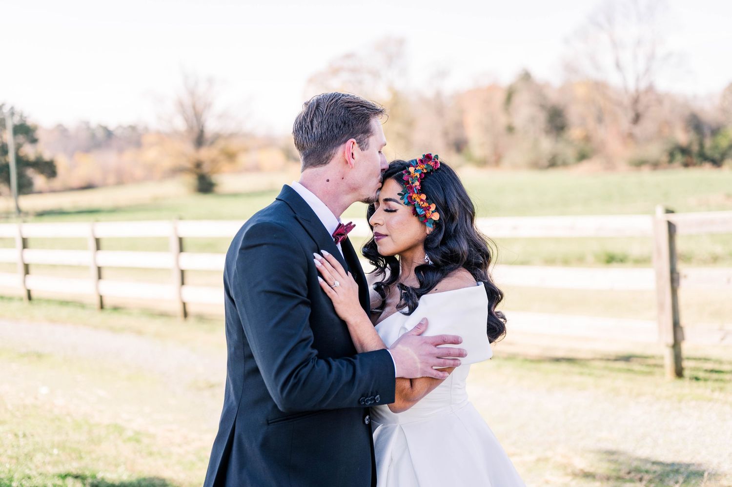 A romantic couple embraces outdoors in front of a rustic wooden fence on their wedding day.