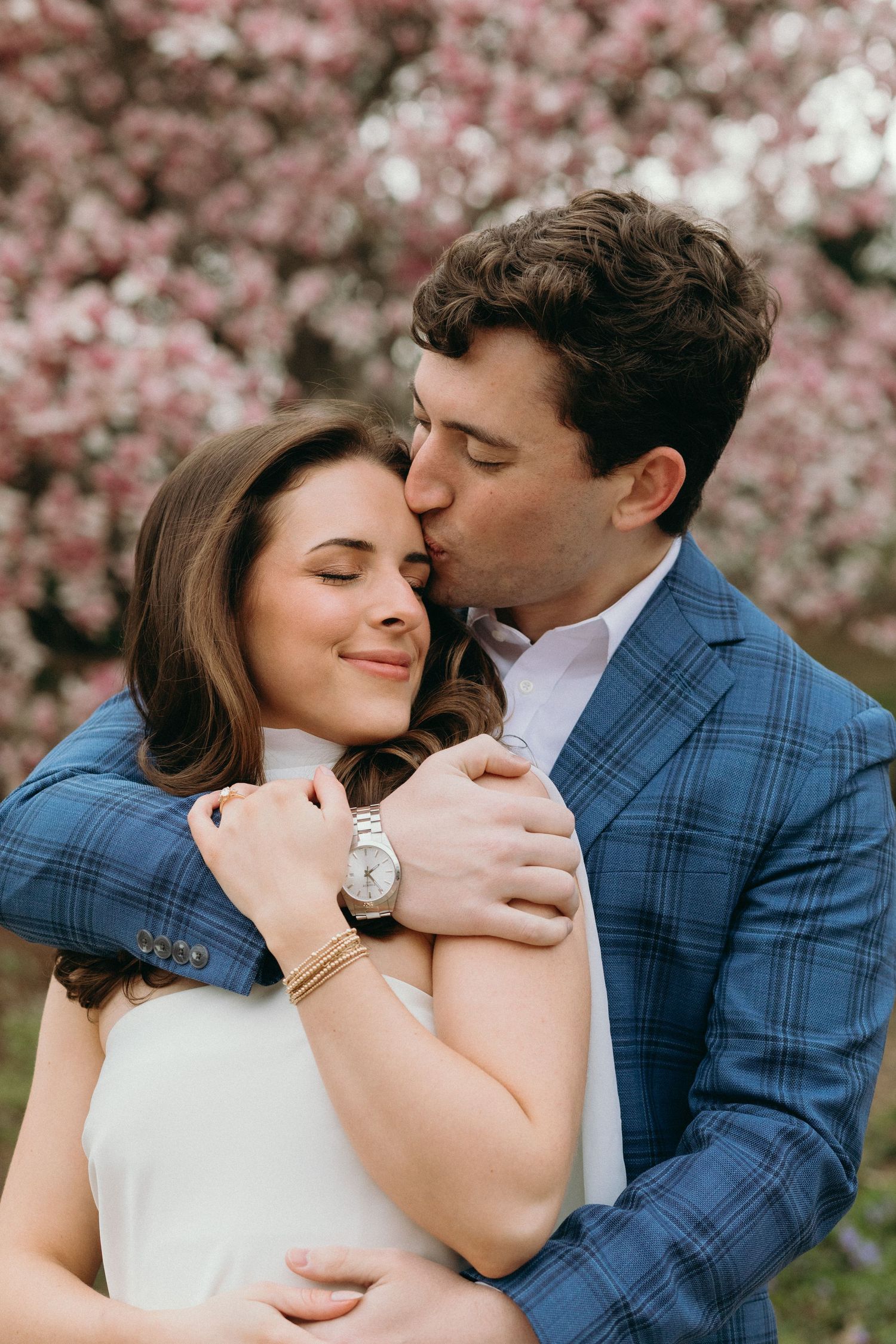 Couple embracing under blooming cherry blossom trees in springtime.