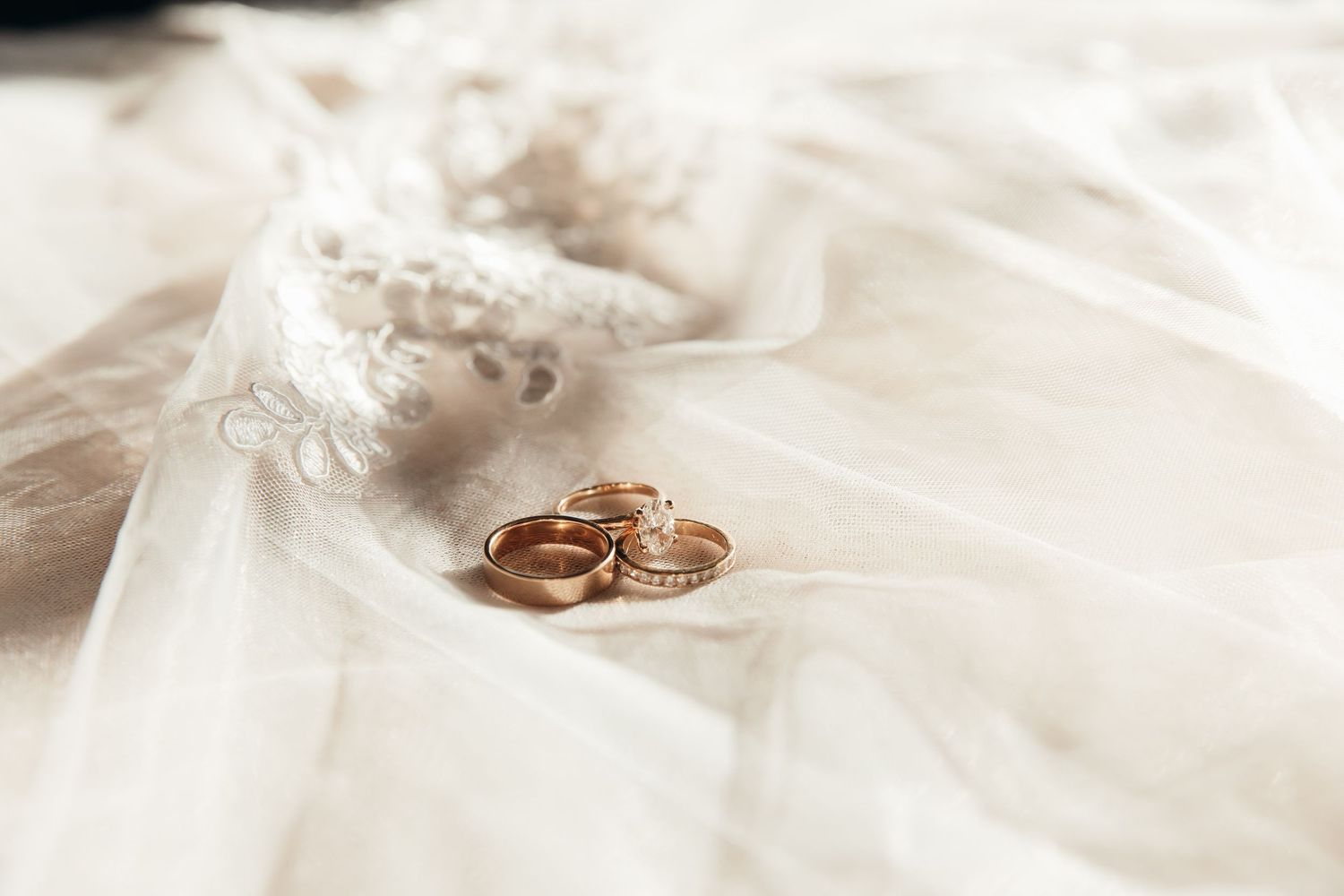 Gold wedding rings rest on delicate white lace against a soft fabric background creating an elegant bridal detail.