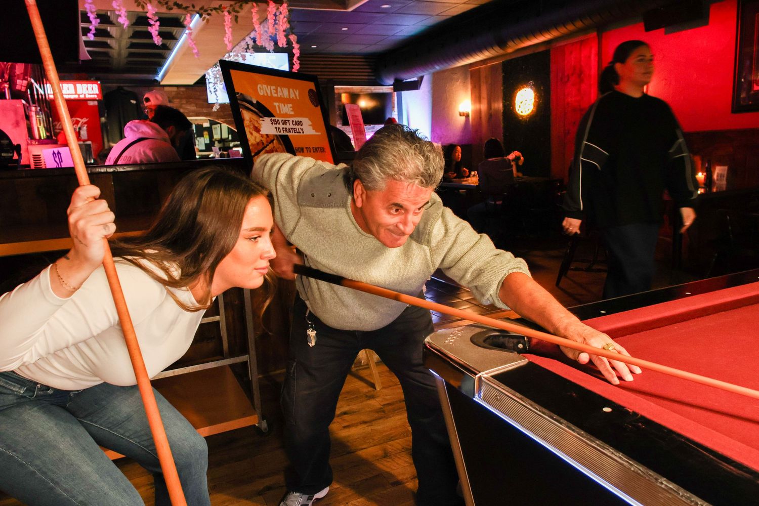 People playing pool game in bar with red walls and wooden floors.