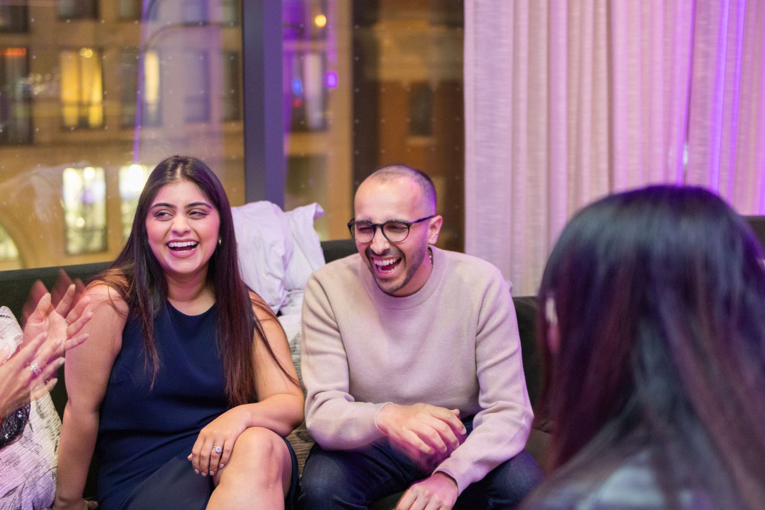 Group of friends laughing and socializing in elegant evening setting with purple lighting.