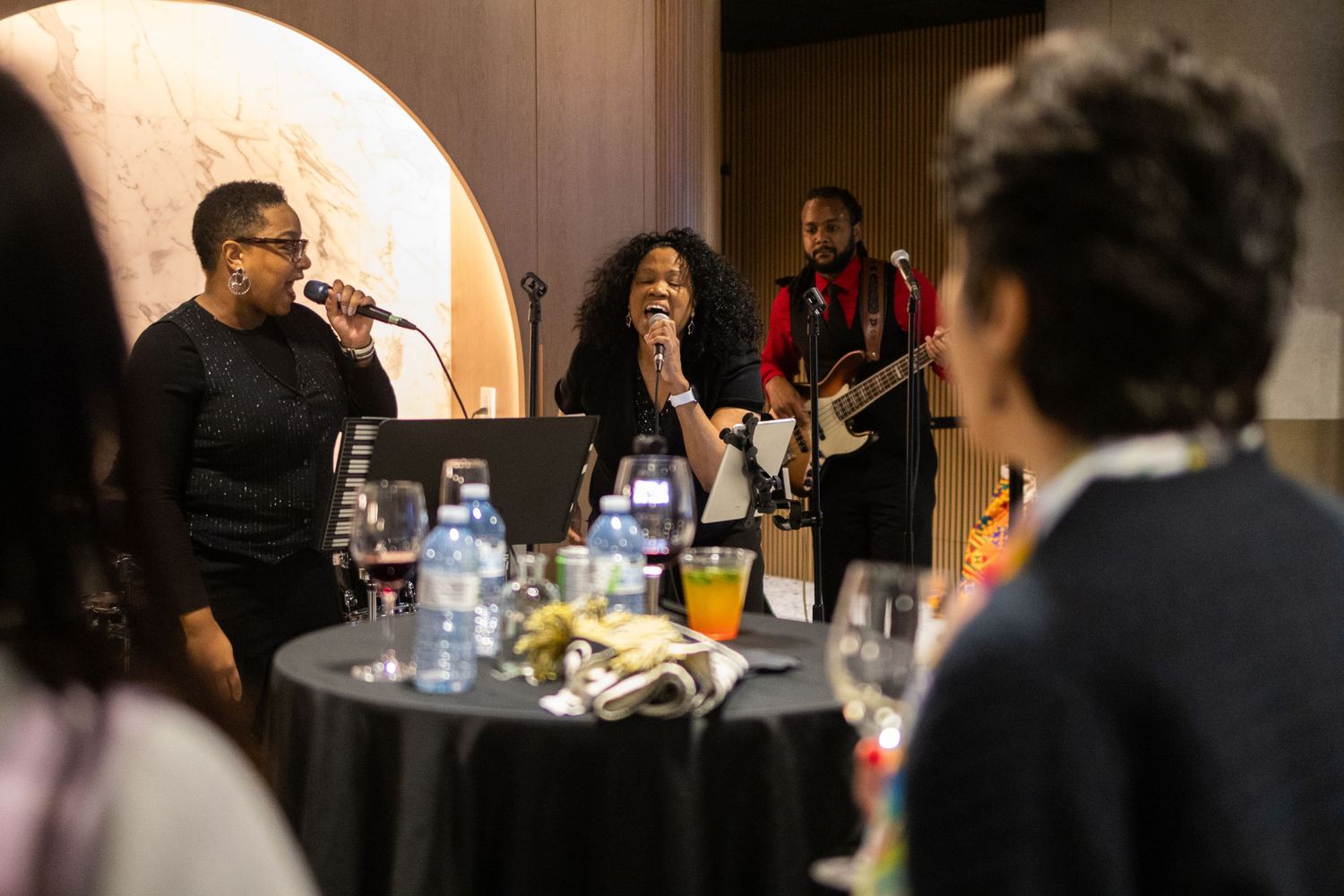 Musicians perform at an intimate dinner venue with tables set with glasses and bottles.