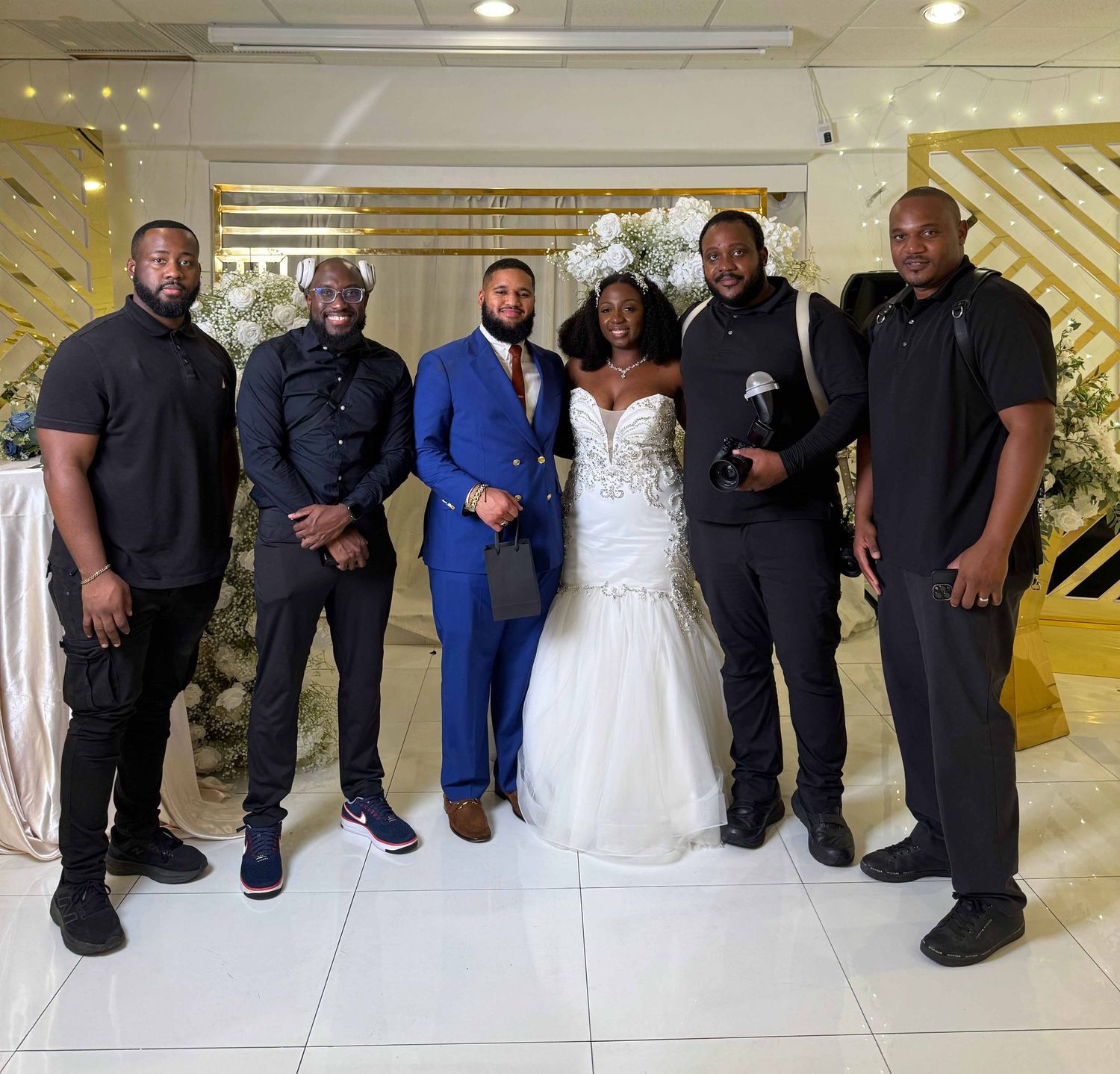 A wedding party poses together in front of a gold and white geometric backdrop during a celebration.