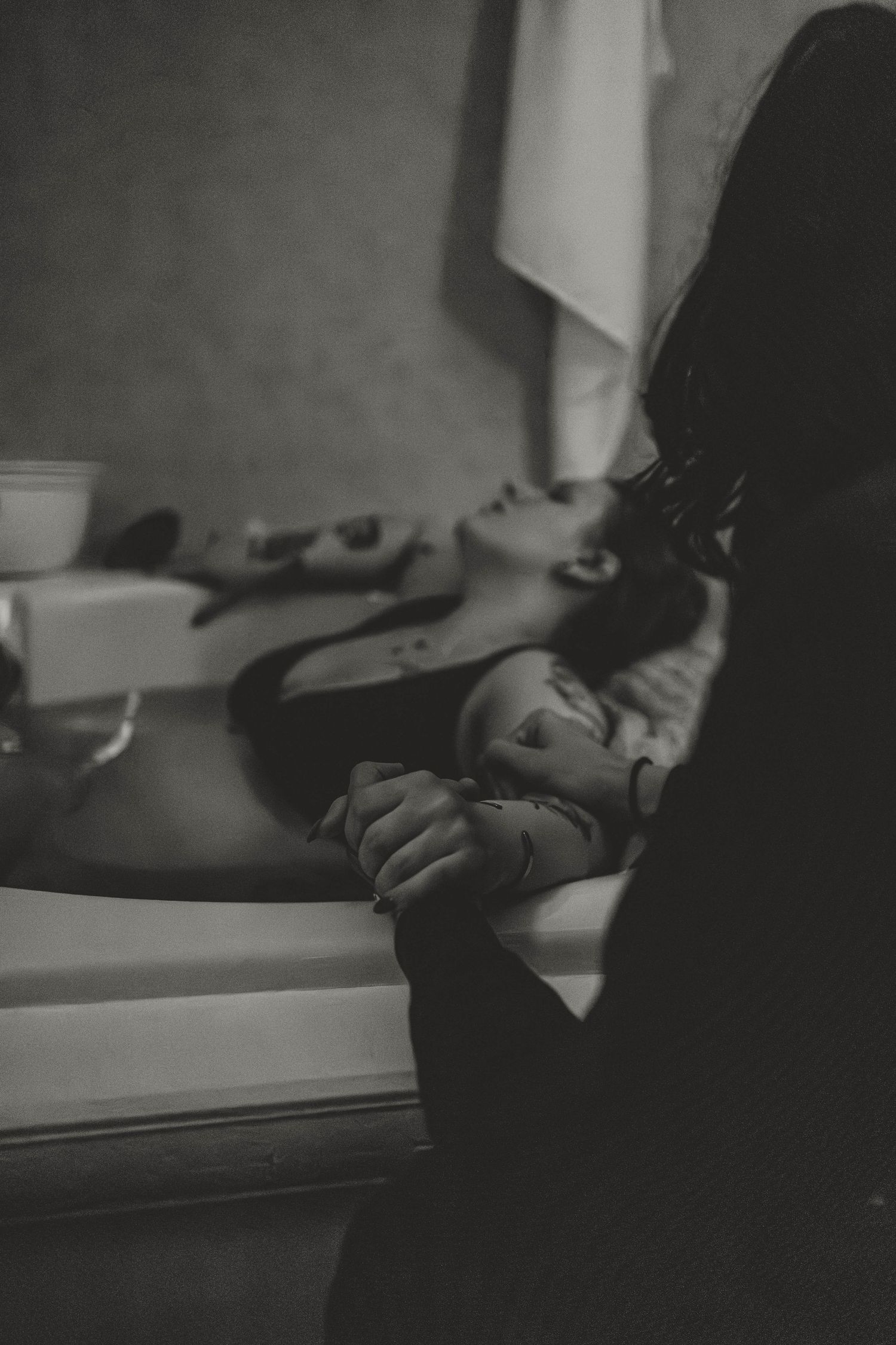 Black and white image of person getting their hair washed at salon basin while laying back in chair.