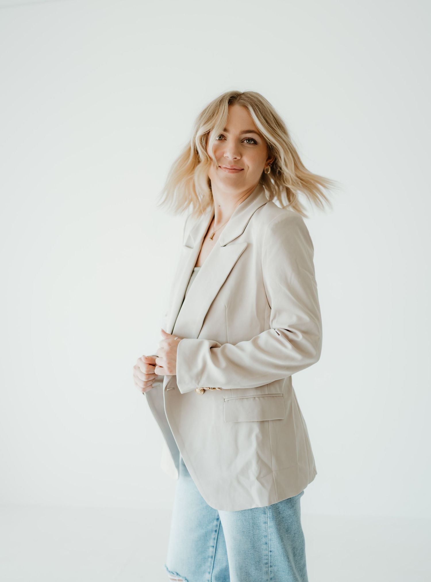 A person in a cream colored blazer and light jeans poses casually against a white background in a photo series.