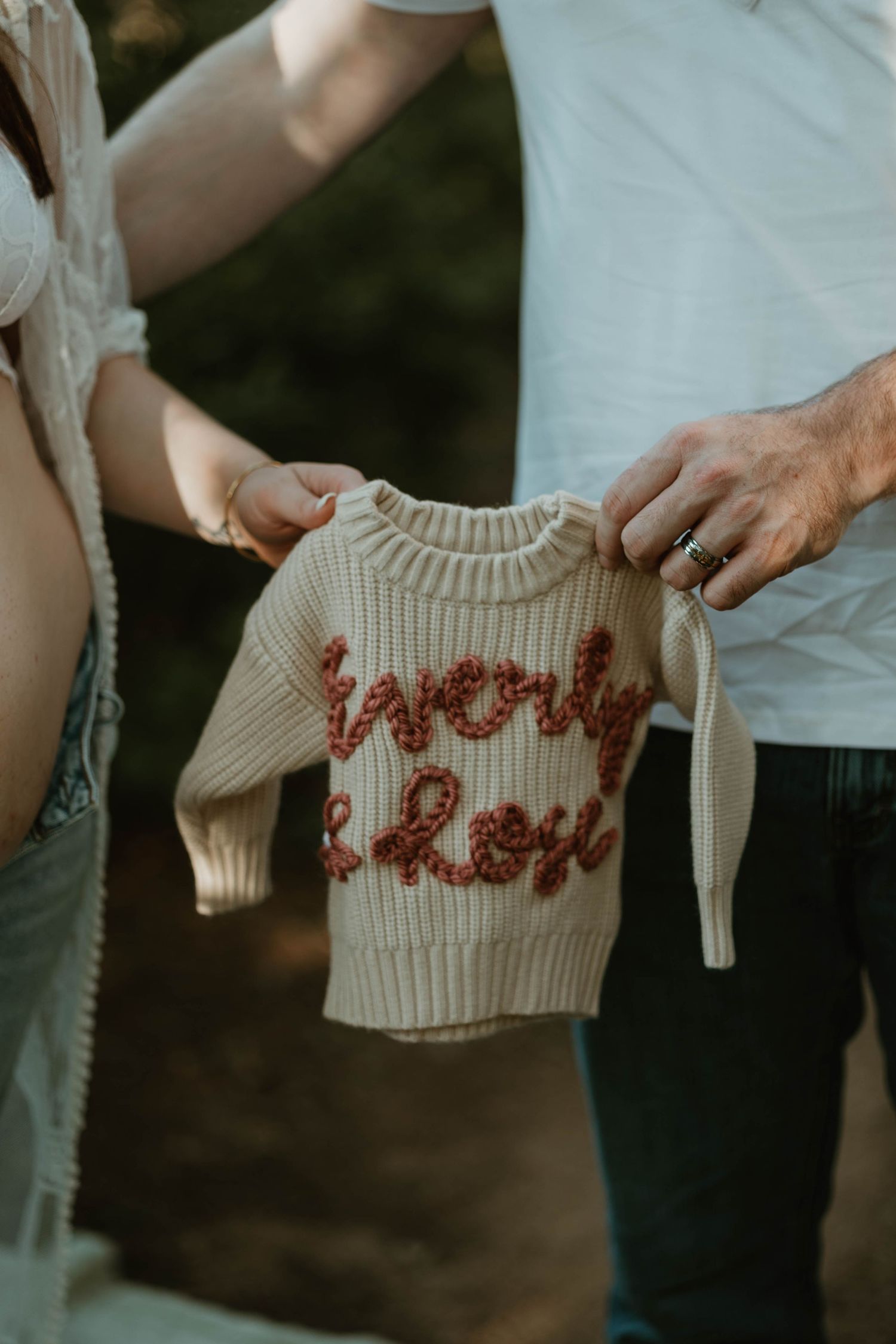 Two hands hold a small cream-colored knit sweater with