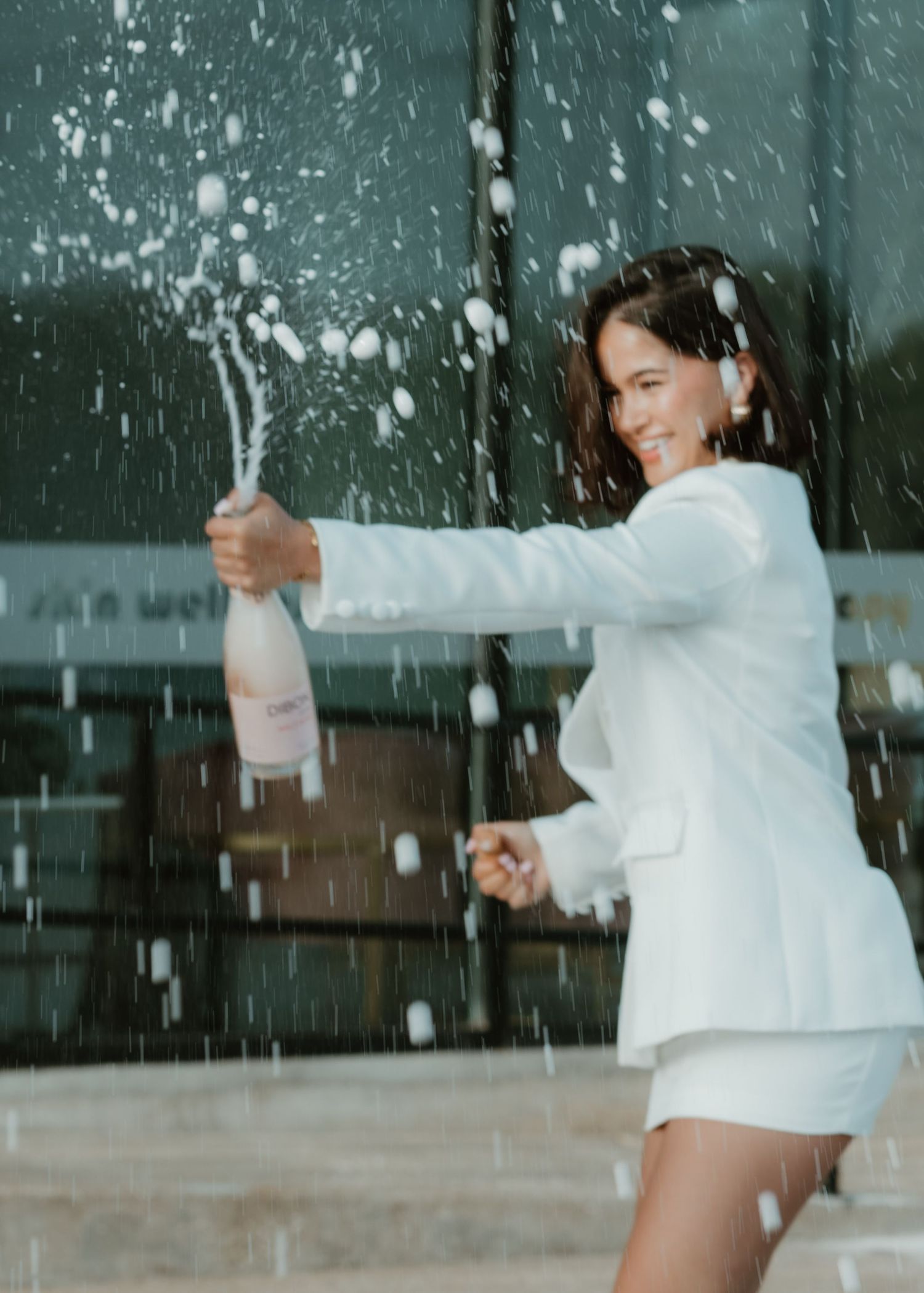 A celebratory moment captured with champagne spray in front of a teal backdrop.