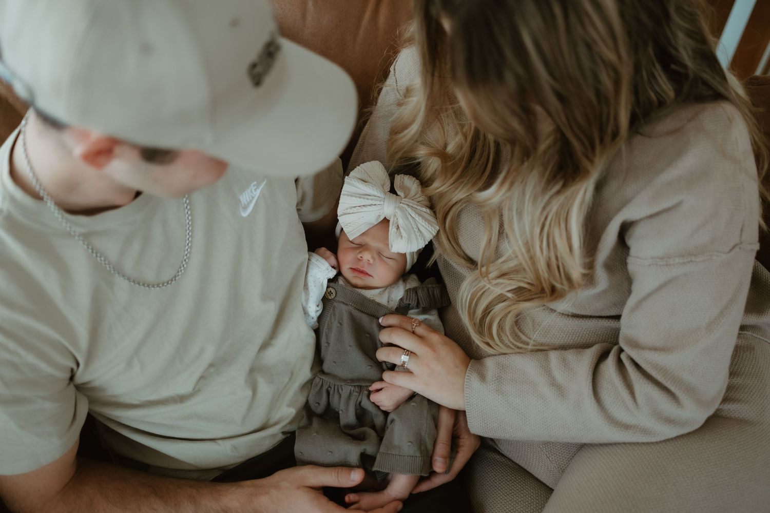 A couple sitting together holds a small baby in a neutral-toned setting.