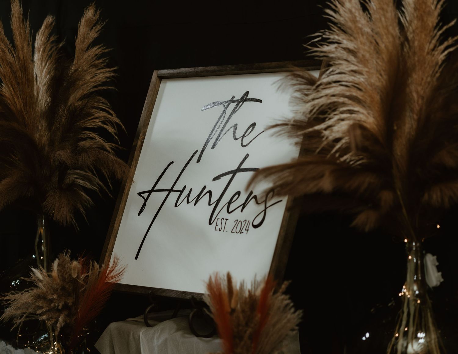 A framed black and white sign reading 'The Hunter' surrounded by brown pampas grass and a glass bottle decoration.
