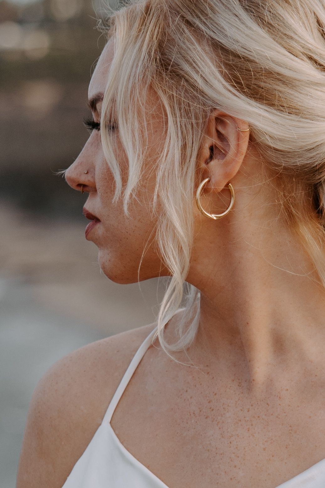 A person with platinum blonde hair styled in an updo wearing hoop earrings, shown from multiple side profile angles.