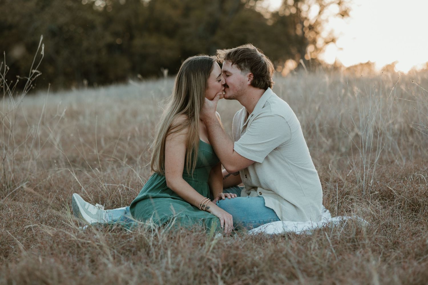 Couple embraces while sitting in a golden field during sunset creating a romantic silhouette.