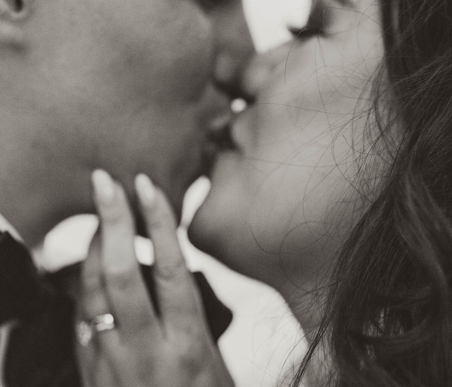 Close-up black and white photo of two people sharing an intimate kiss with delicate fingers gently touching.